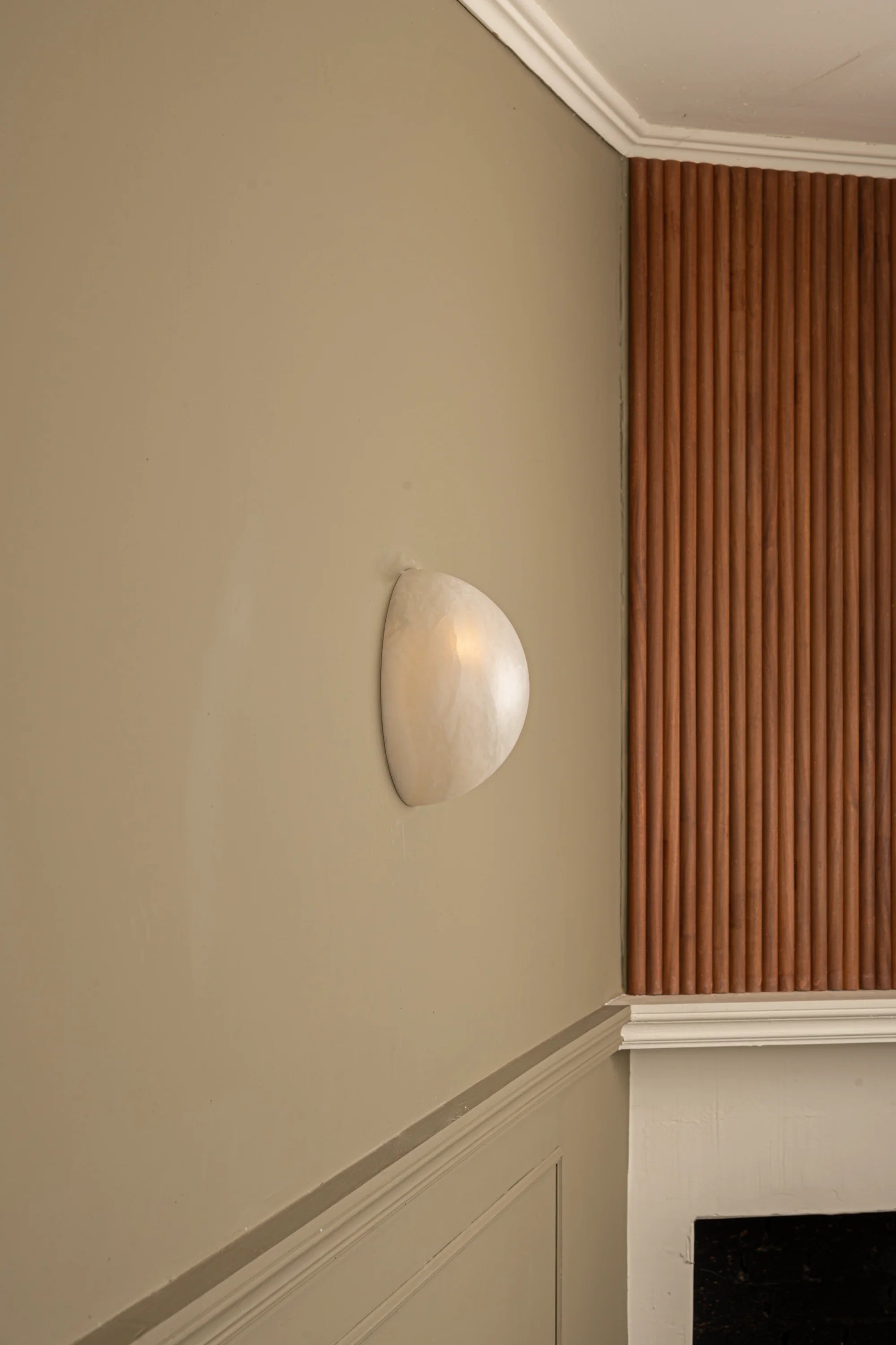Wall-mounted light fixture on a beige wall with wooden paneling.