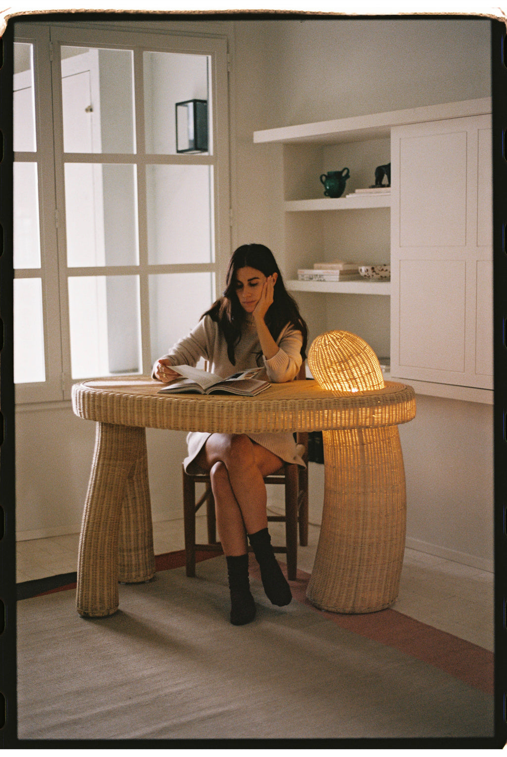 Heaps & Woods Asahan Desk, a distinctive organic modern desk crafted from natural woven rattan in a warm light brown finish, featuring a round tabletop and two sculptural, tapered legs, one of which uniquely integrates an ambient light source. This contemporary rattan writing desk is perfect for a coastal home office, bohemian living room, or as a statement entryway console.