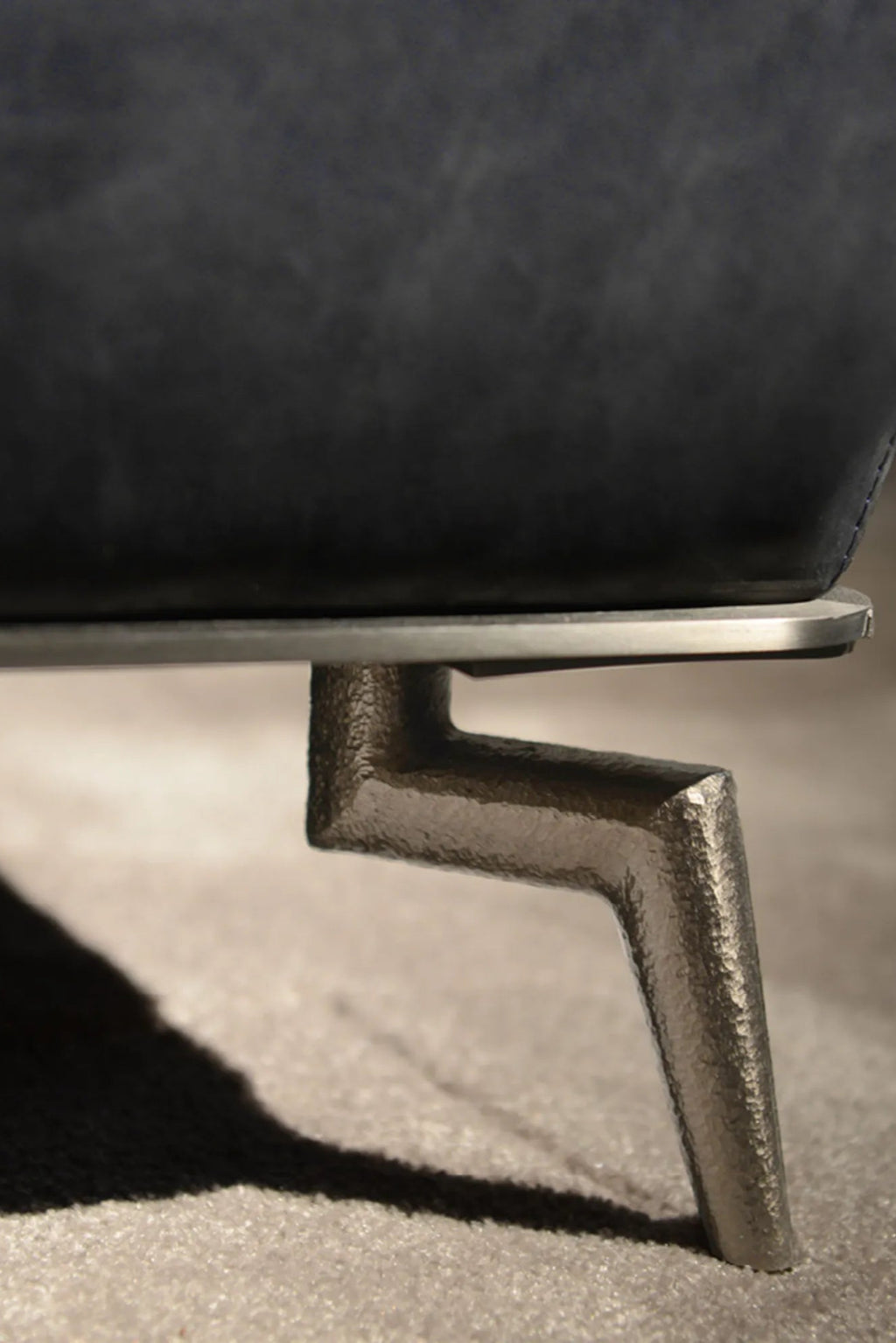 Hessentia Janet Armchair, a contemporary lounge chair featuring rich charcoal grey distressed upholstery with a sleek dark metal base and a distinctive angled, hammered bronze metal leg. This modern armchair offers an industrial chic aesthetic, perfect for a sophisticated living room or stylish home office.