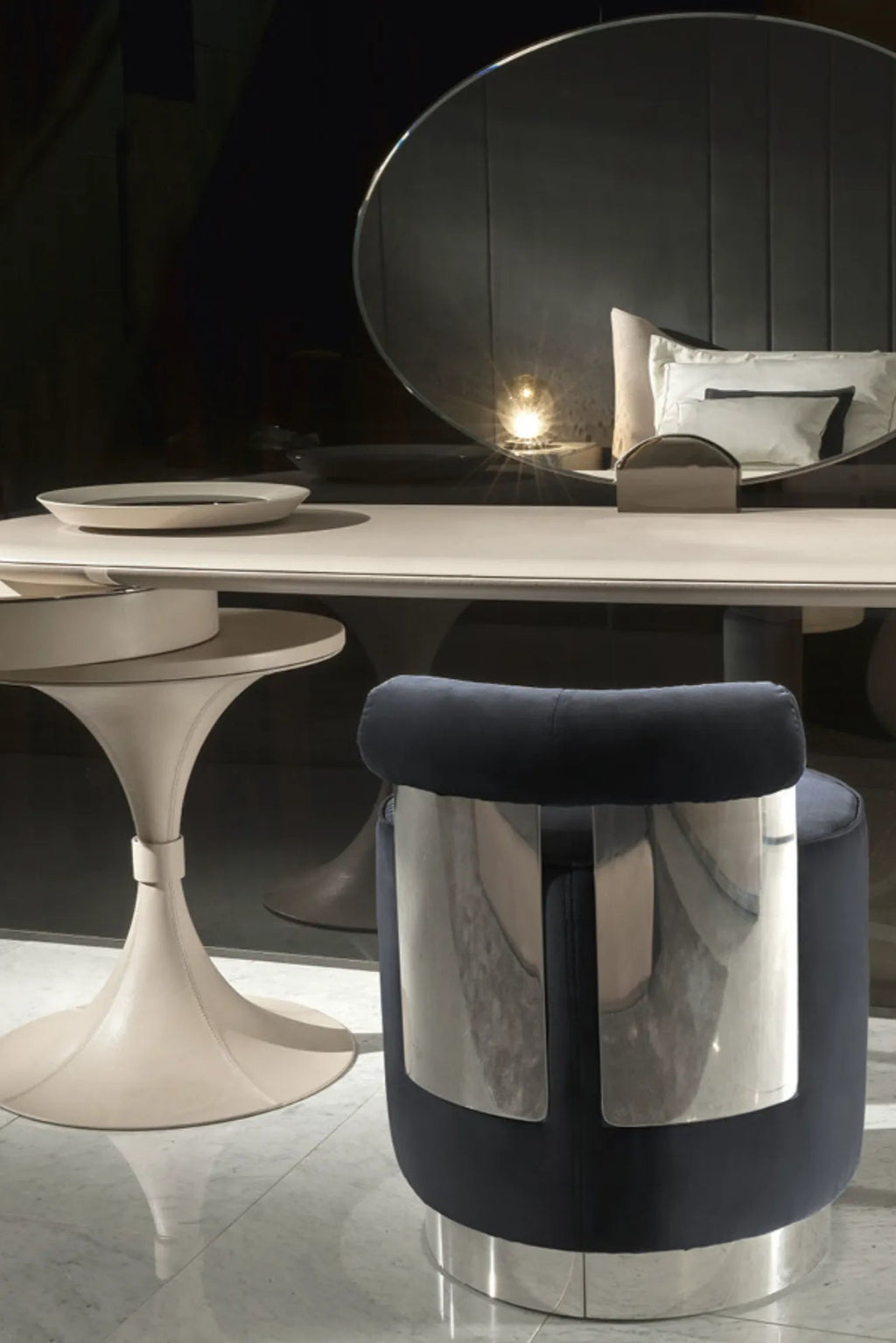 Hessentia Shelly Pouf, a contemporary cylindrical accent stool upholstered in rich dark blue velvet fabric with a gleaming polished chrome base and striking vertical chrome backrest details. This modern luxury pouf is perfect as a stylish vanity stool or glamorous accent seating in a bedroom or living room.