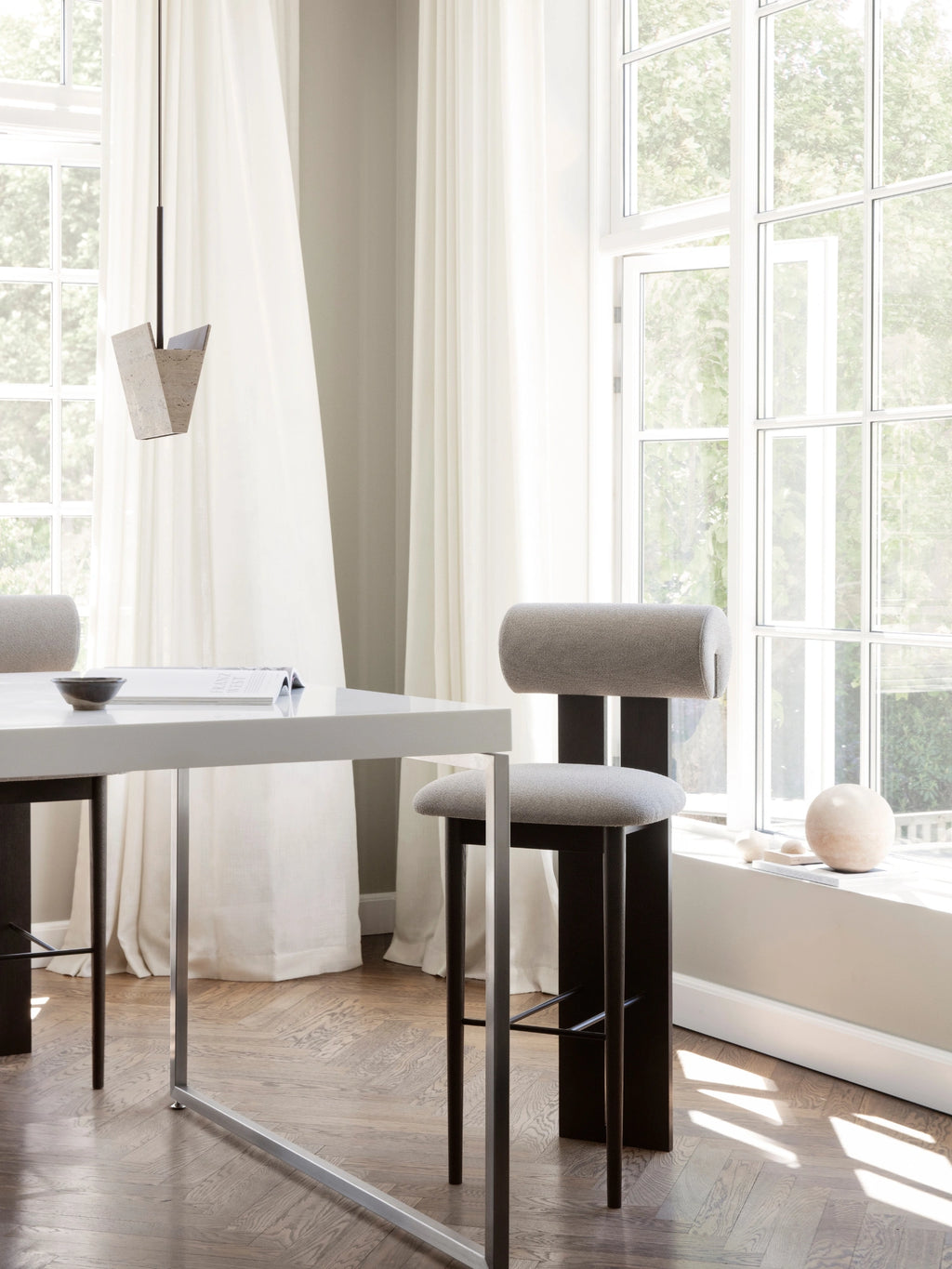 NORR11 Hippo Bar Chair, a modern sculptural bar stool featuring a bold dark wood frame with a distinctive cylindrical light grey upholstered backrest and matching seat, complemented by a sleek matte black metal footrest. This minimalist design bar chair offers contemporary kitchen island seating or stylish bar area furniture for sophisticated interiors.