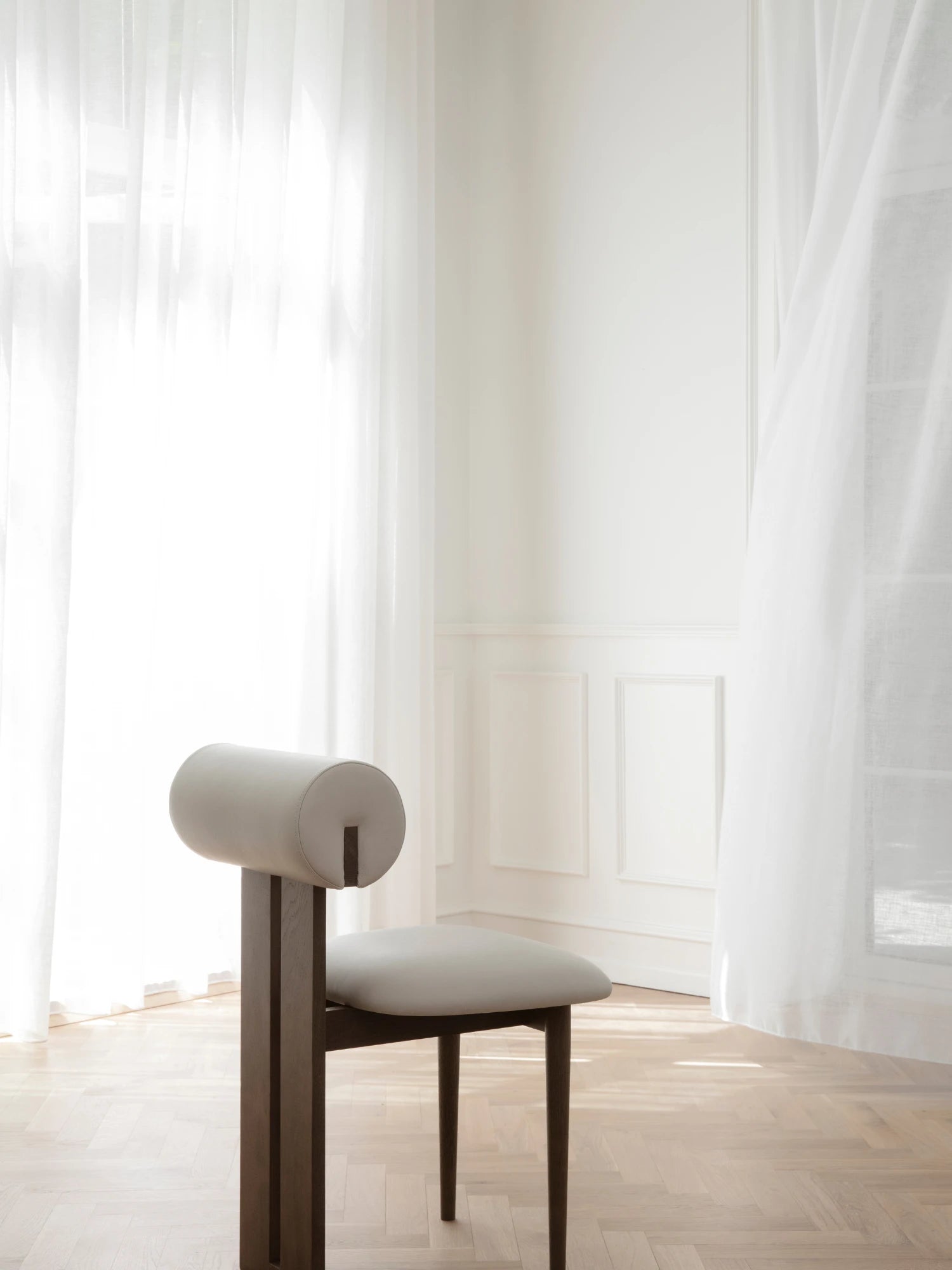NORR11 Hippo Chair, a striking organic modern dining chair featuring a dark stained solid oak wood frame with a light greige leather upholstered seat and a unique cylindrical bolster backrest. This sculptural wood chair offers a minimalist design, perfect for contemporary dining rooms, elegant living room accents, or sophisticated home office furniture.