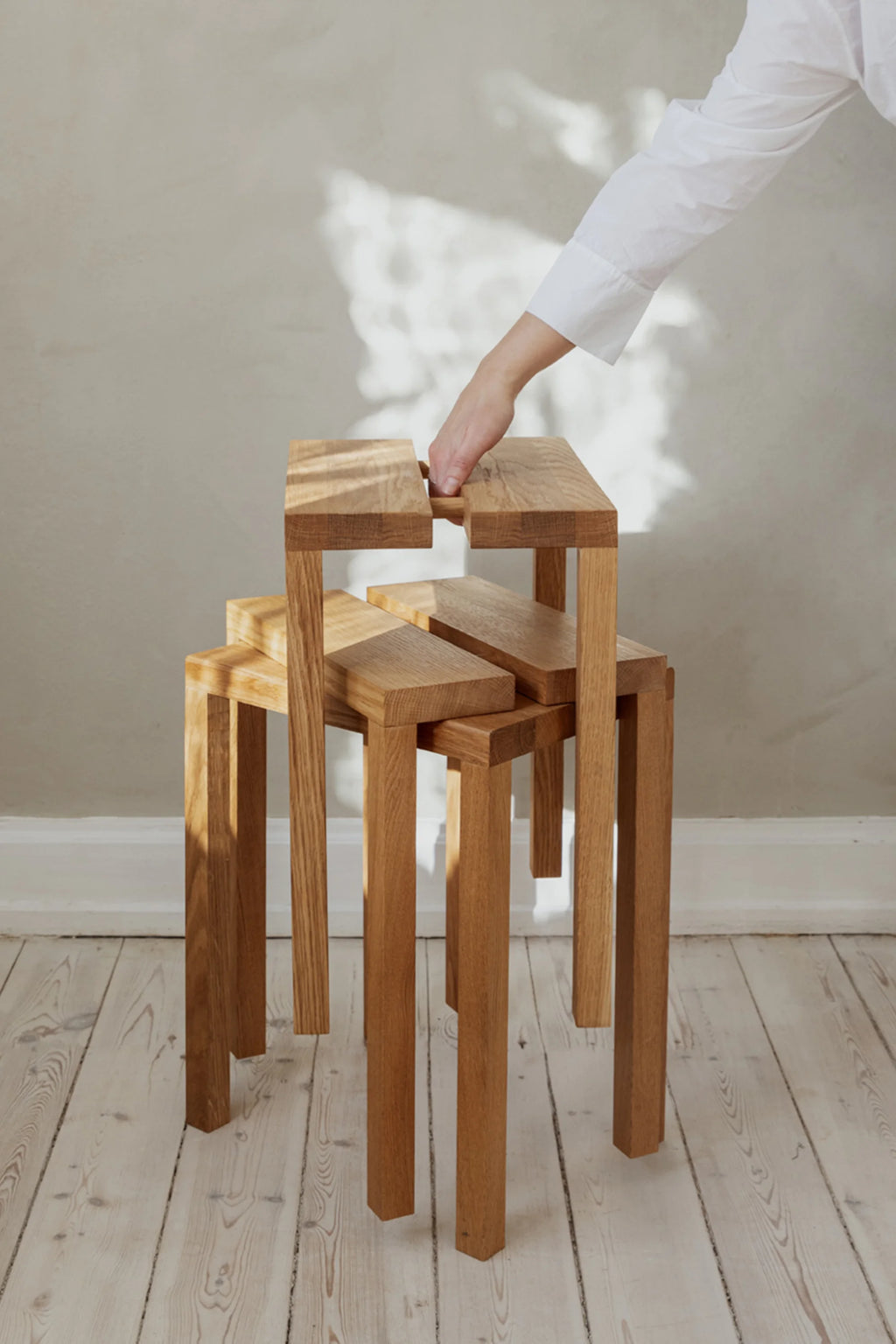 MOEBE Peg Stool, a modern minimalist solid oak stool featuring a unique interlocking modular design with warm natural wood tones and visible grain. This versatile Scandinavian wood stool can be used individually or stacked as a flexible side table for small living rooms or contemporary bedrooms.