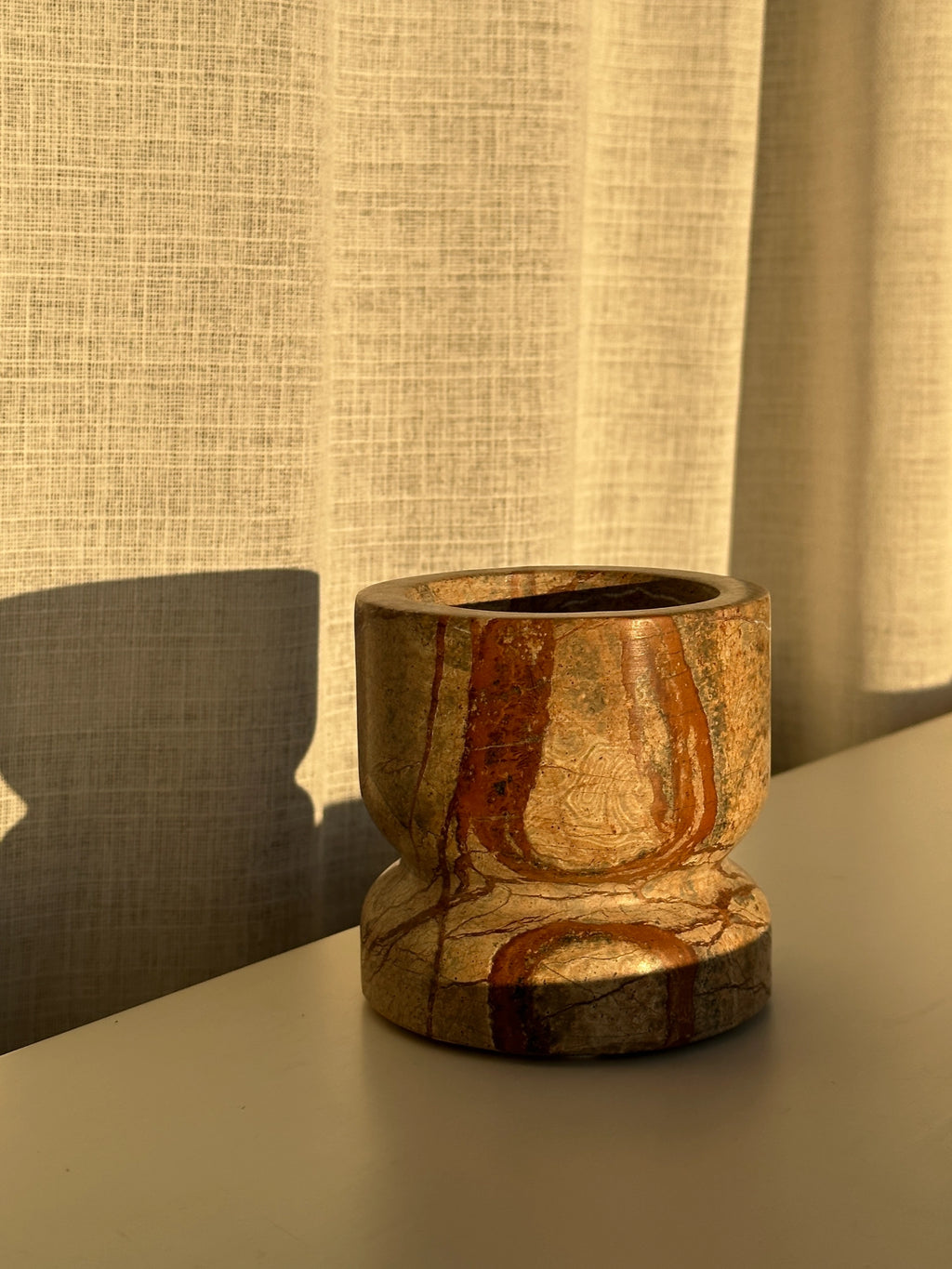 Tinted Objects Dahl Bowl, a unique decorative bowl crafted from natural stone with earthy brown, cream, and reddish-orange veining, featuring a rounded, hourglass-like silhouette. This elegant and versatile accent piece is perfect for adding organic texture to modern home decor.
