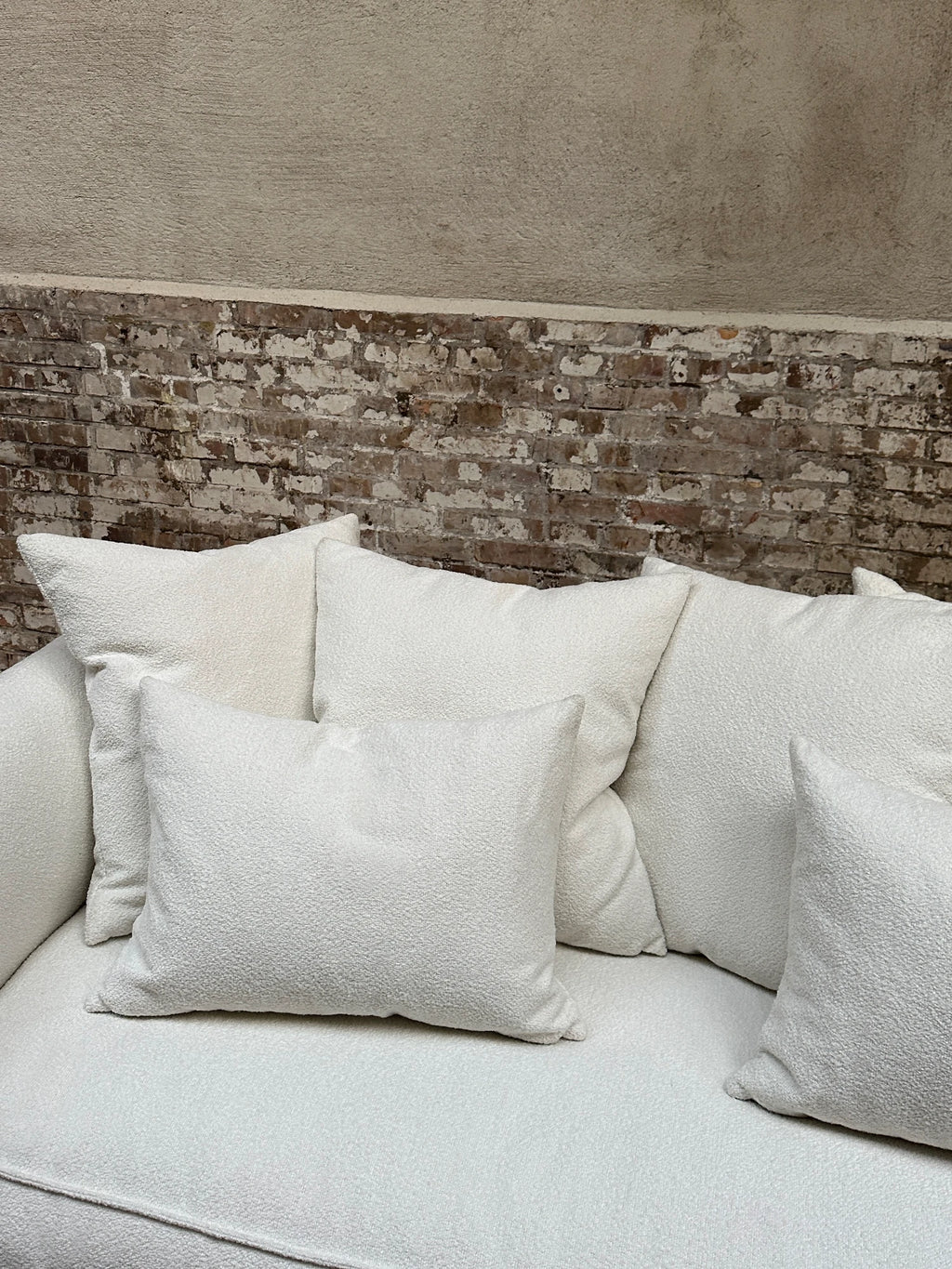 Tinted Objects Cornell Sofa, a luxurious off-white textured fabric sofa with plush cushions, set against a rustic exposed brick wall. This elegant modern sofa is perfect for creating a cozy and stylish living space for contemporary homeowners.