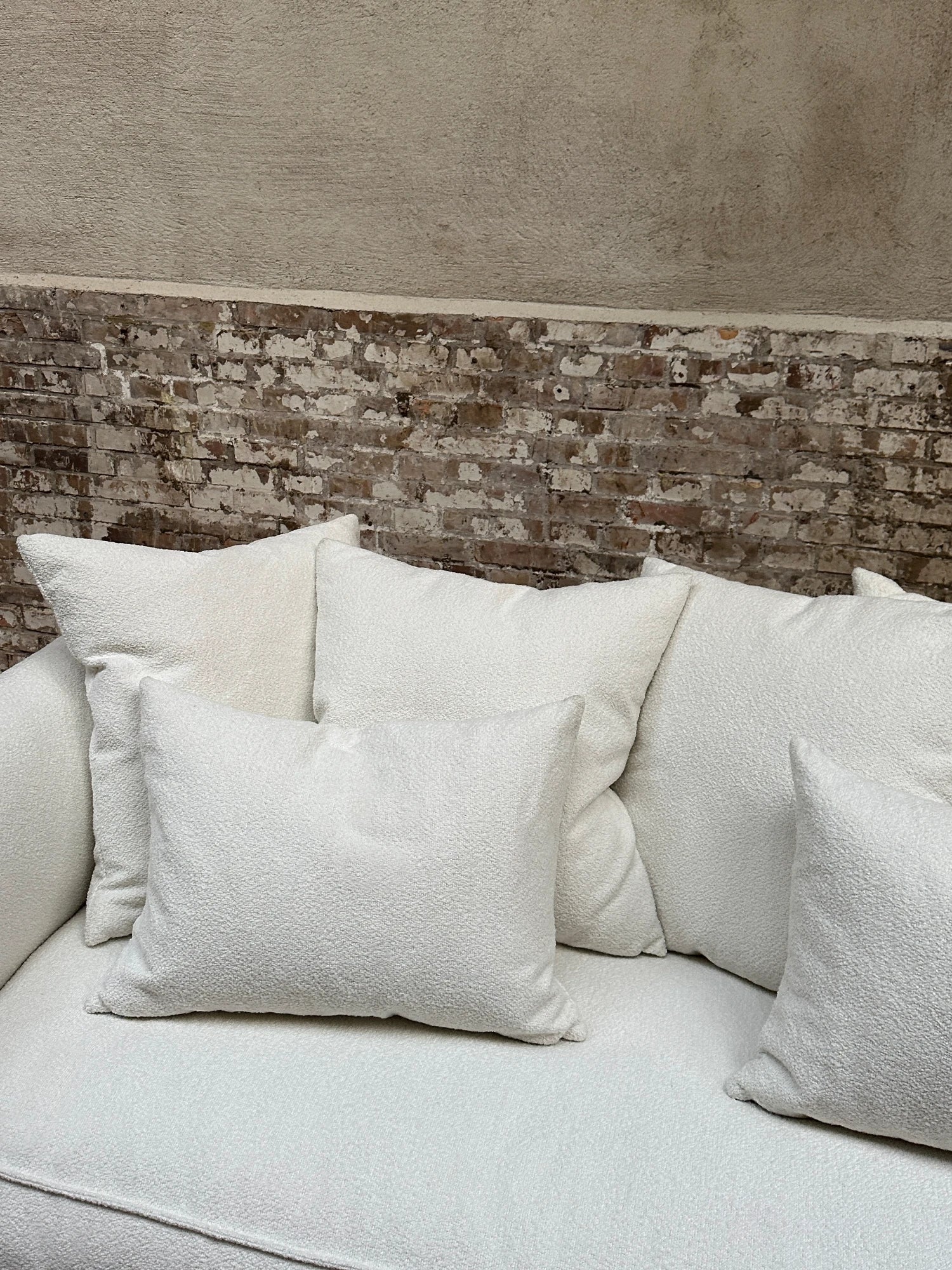Tinted Objects Cornell Sofa, a luxurious off-white textured fabric sofa with plush cushions, set against a rustic exposed brick wall. This elegant modern sofa is perfect for creating a cozy and stylish living space for contemporary homeowners.