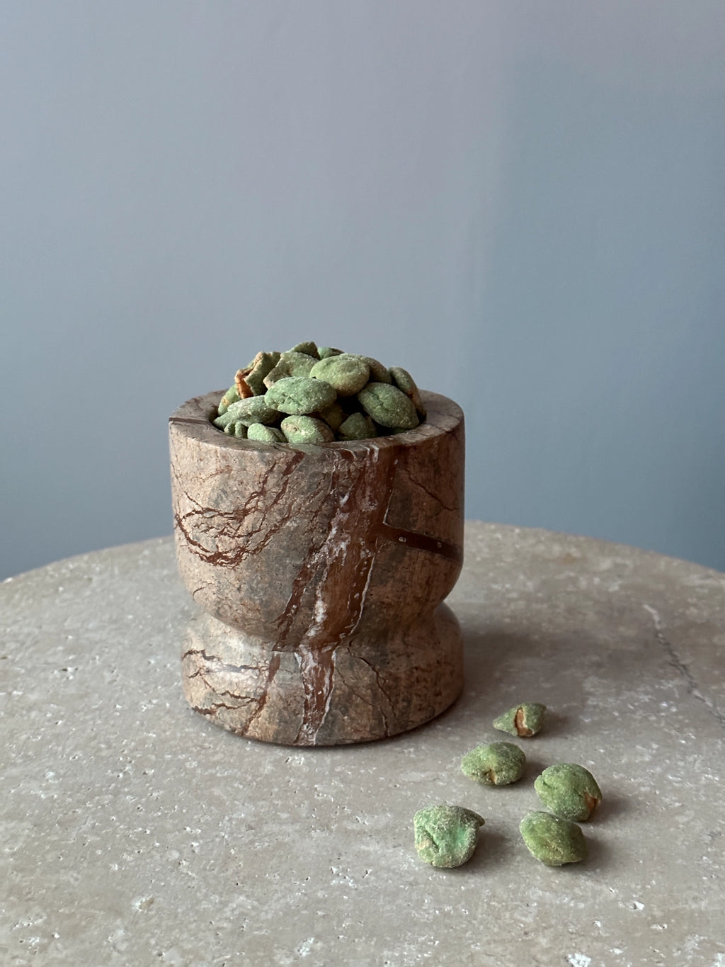Tinted Objects Dahl Bowl, a unique decorative bowl crafted from natural brown marble with striking dark brown veining and a distinctive hourglass shape, filled with green snacks. This elegant marble bowl is perfect for adding a touch of natural luxury to any modern home decor or serving small treats.