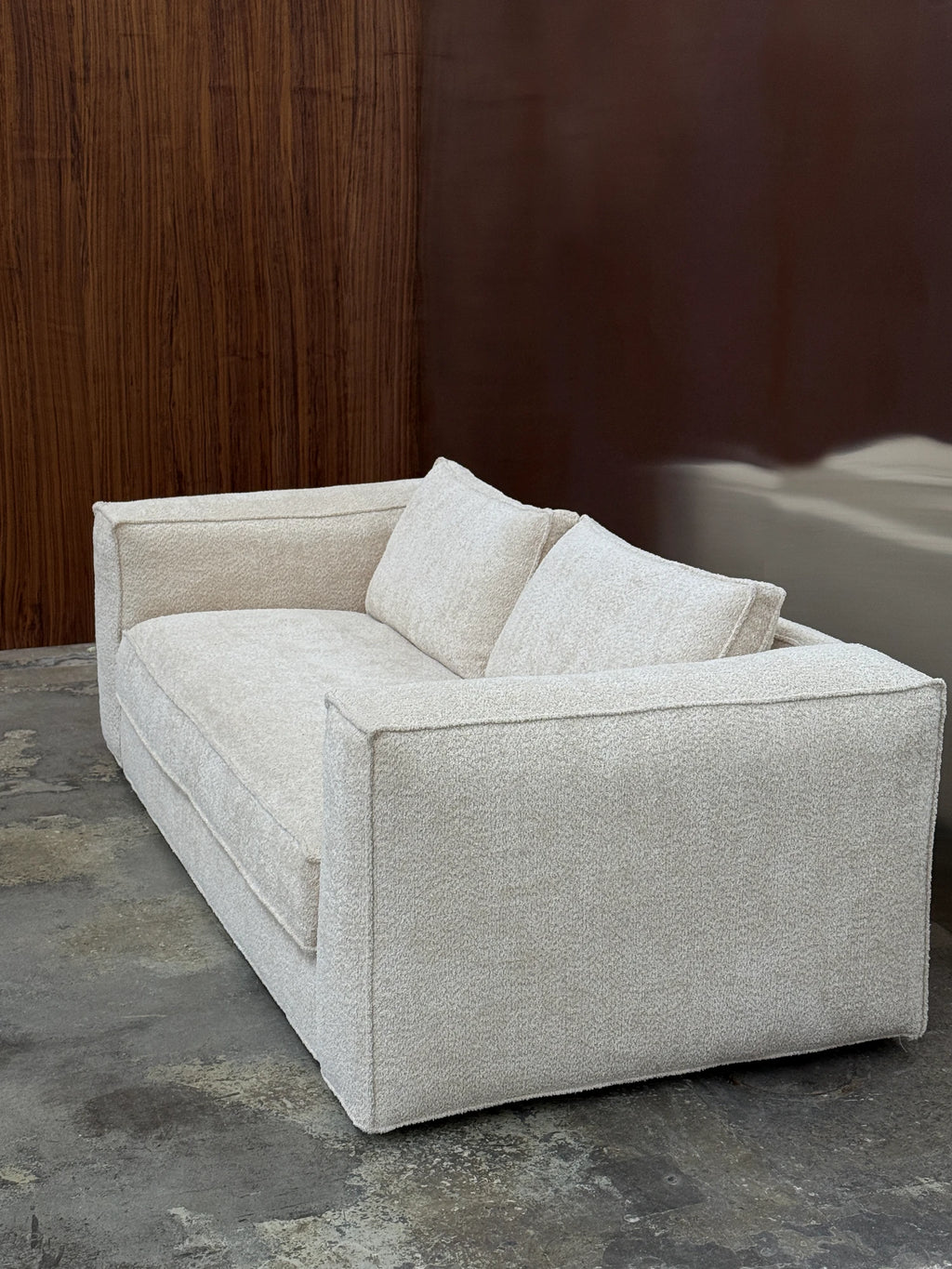 Tinted Objects Klinge Sofa, a modern two-seater sofa upholstered in a light beige, textured bouclé fabric with clean lines and two matching throw pillows. This contemporary couch is perfect for adding stylish comfort to a minimalist living room or cozy lounge area.