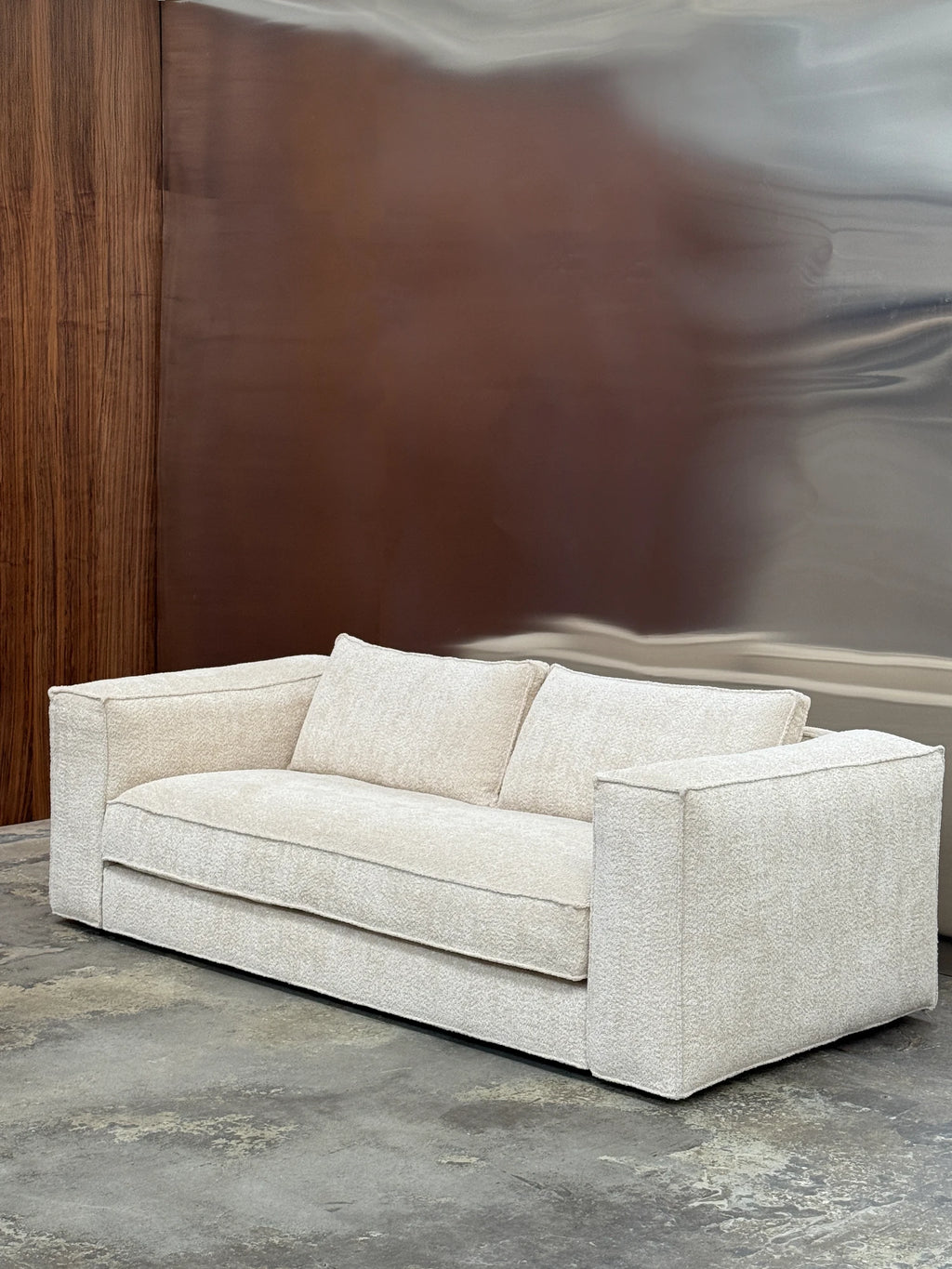 Tinted Objects Klinge Sofa, a modern minimalist 2-seater sofa upholstered in a rich, cream-colored textured boucle fabric with a low-profile, rectilinear silhouette. This contemporary couch features wide, structured arms and plush cushions, offering a clean, inviting aesthetic. Perfect for modern living rooms, minimalist apartments, or cozy, design-conscious spaces.
