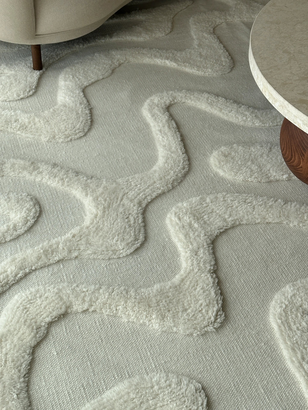 Tinted Objects Norlander Wool Rug, featuring a modern, abstract wavy pattern with plush, textured ivory wool loops on a flat woven cream base. This luxurious and durable area rug is perfect for adding warmth and sophisticated style to contemporary living rooms or bedrooms.