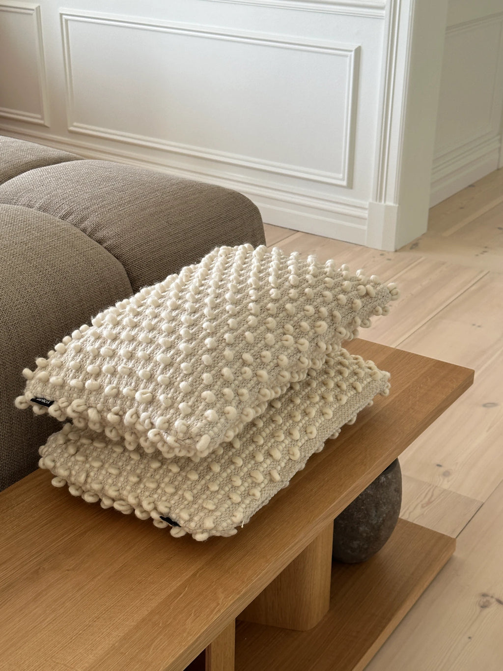 Tinted Objects Tuhlin Throw Pillow, two stacked modern decorative cushions with a light beige knitted texture and off-white bobble accents. These stylish accent pillows are perfect for adding cozy comfort and contemporary design to a living room sofa or bedroom for discerning interior decorators.