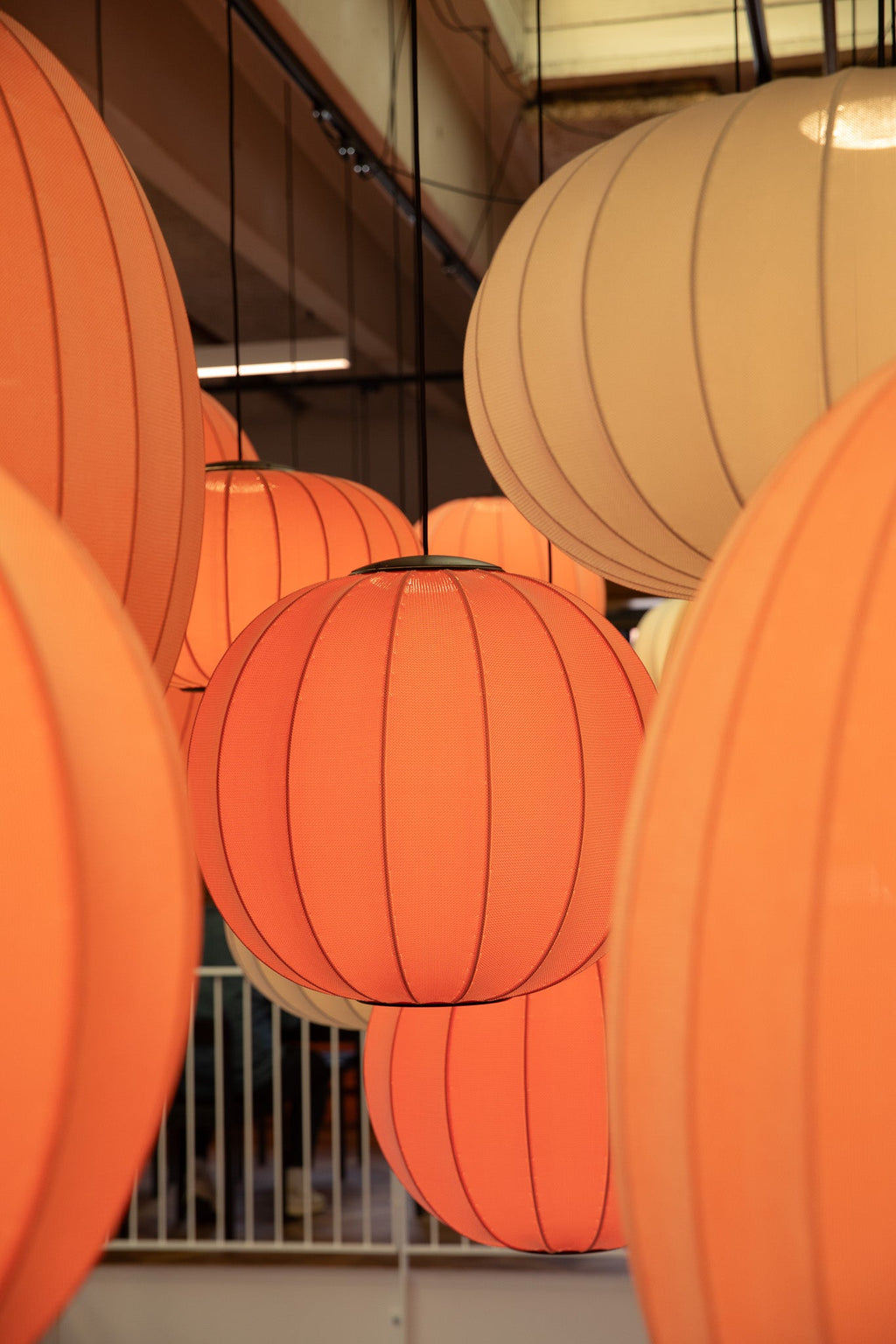 Made by Hand Knit-Wit Ø60 Round Pendant Lamp, a modern Scandinavian ceiling light crafted from a unique knitted textile fabric in a warm orange hue, featuring a distinctive spherical shape with visible vertical ribs. This contemporary pendant lamp, also seen in a soft beige, offers ambient illumination and a cozy texture. Ideal for creating inviting lighting in living rooms, dining areas, or modern bedrooms.