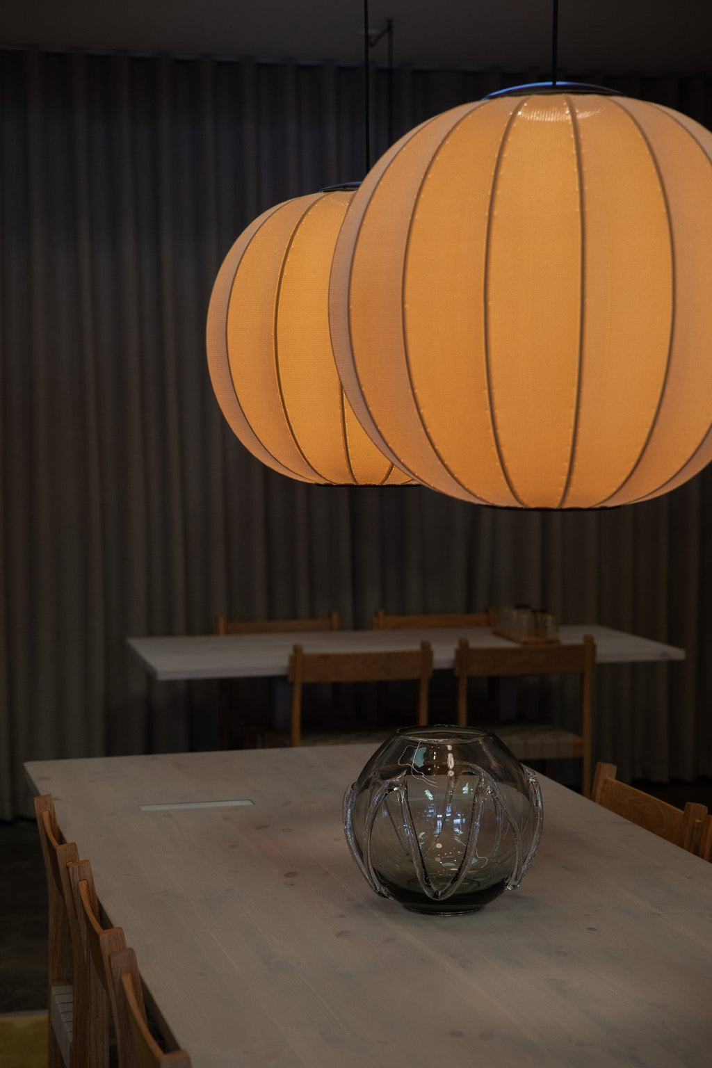 Made by Hand Knit-Wit Ø60 Round Pendant Lamp, a large spherical textile pendant light glowing with a warm orange hue, featuring a unique knitted fabric shade stretched over a ribbed frame. This contemporary Scandinavian design offers soft, diffused illumination, creating a cozy ambiance. Ideal for modern dining rooms, living spaces, or bedrooms seeking an organic modern aesthetic.
