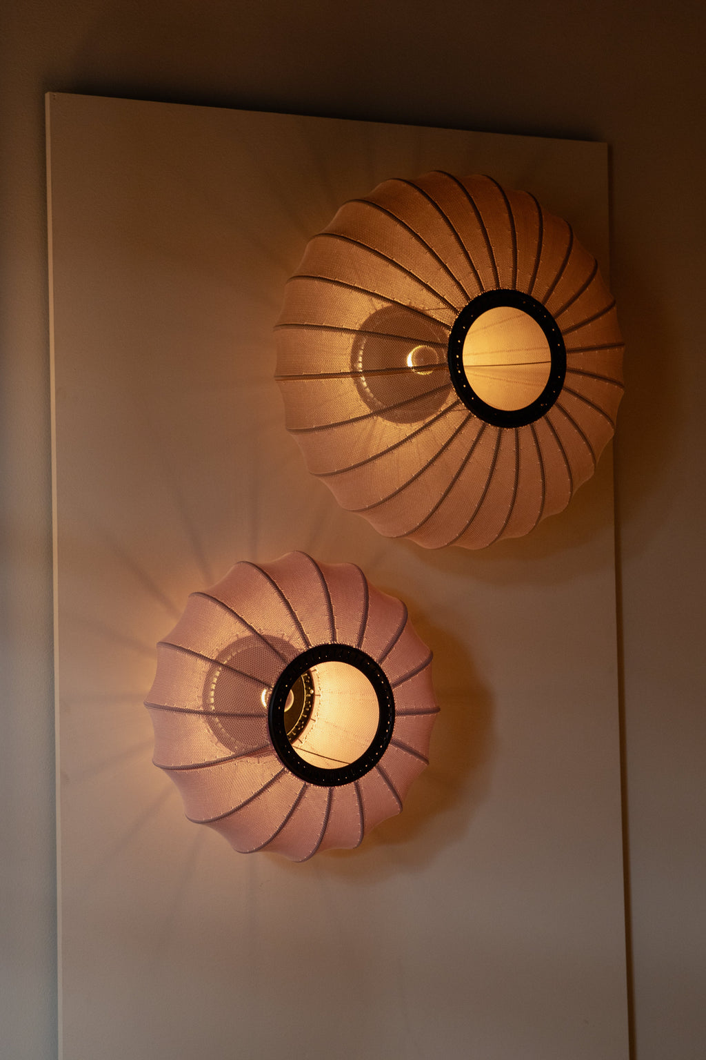 Made by Hand Knit-Wit Ø45 Oval Wall Light, a set of two contemporary organic modern wall sconces featuring fluted knitted textile diffusers in warm peach and soft blush pink, with a central matte black metal ring. These decorative wall lights cast a cozy, ambient glow, perfect for Scandinavian living rooms, serene bedrooms, or inviting hallways.