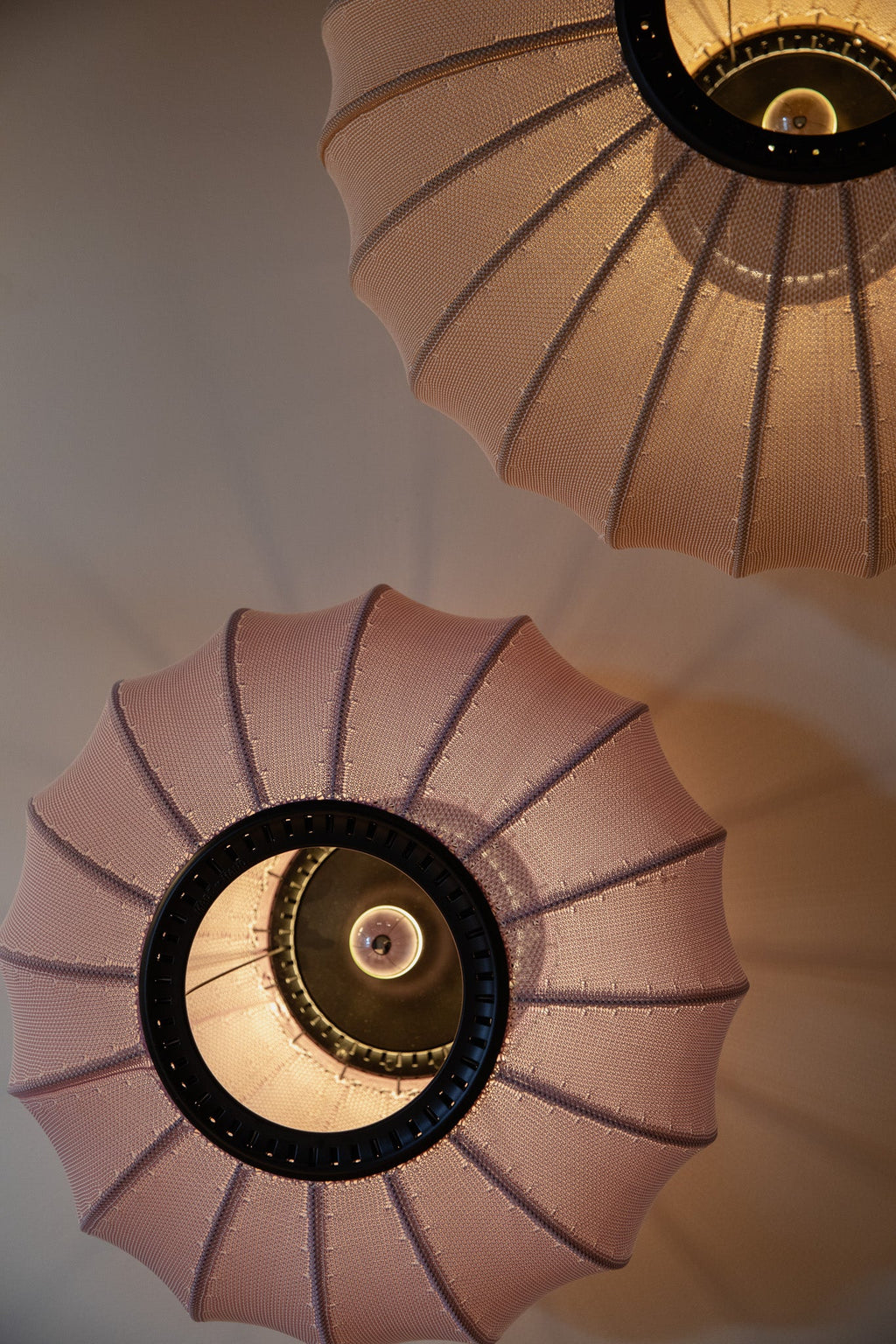 Made by Hand Knit-Wit Ø45 Oval Wall Light, a modern Scandinavian wall light featuring a unique blush pink knitted fabric shade with a ribbed, pleated texture and a distinct oval, organic silhouette. This contemporary textile lighting piece casts a soft, warm glow, enhanced by its dark metal inner frame. Ideal as a stylish bedroom accent, cozy living room wall lamp, or designer entryway lighting for modern minimalist and organic modern interiors.