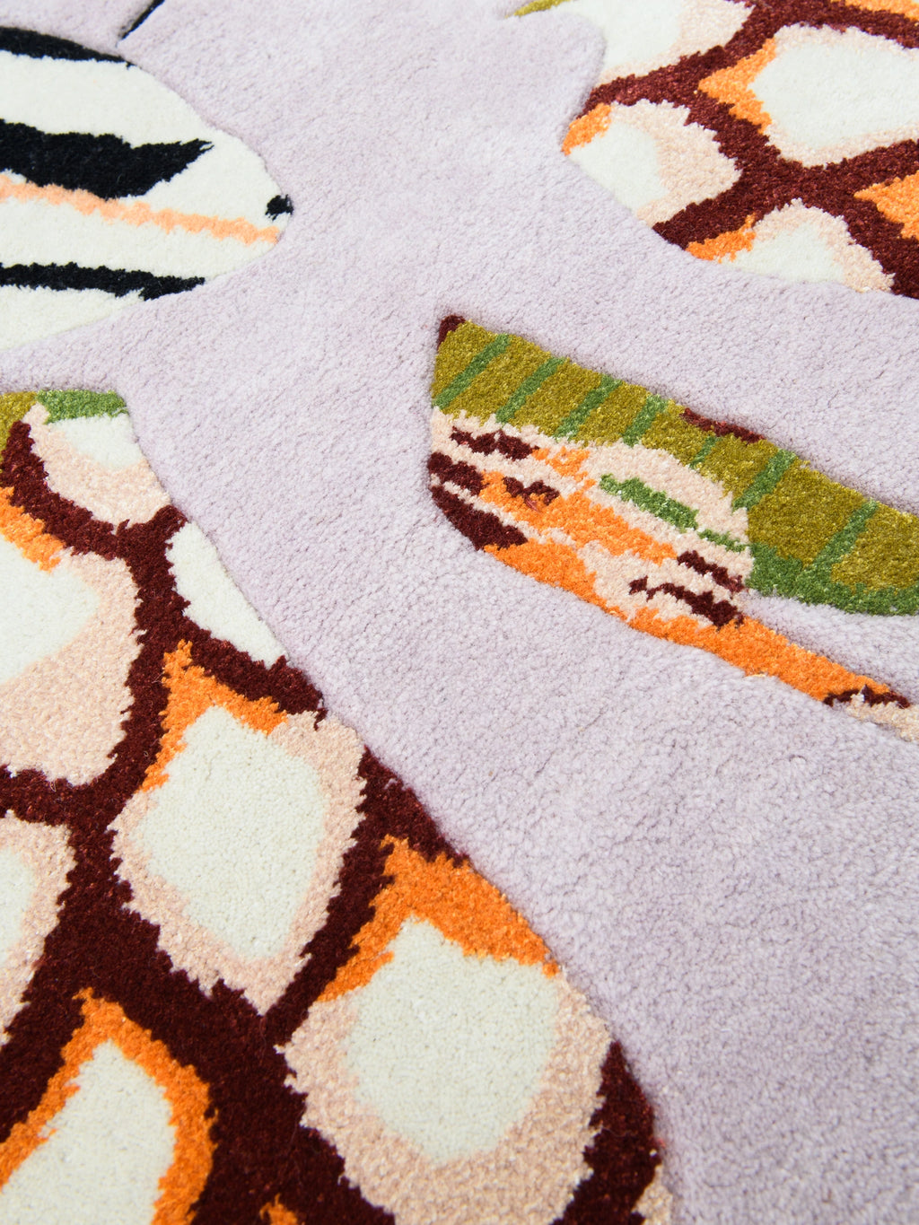 Haus Üger Insecta Rug, a vibrant hand-tufted wool rug featuring a soft lilac background and plush texture with varying pile heights. It showcases large, abstract organic shapes in a striking color palette of cream, bright orange, rich brown, black, and olive green, reminiscent of a nature-inspired insect wing pattern. This maximalist area rug is perfect for adding a playful modern aesthetic to a contemporary living room, creative studio, or a child's bedroom.
