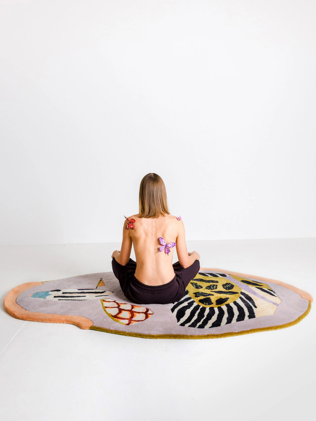 Haus Üger Insecta Rug, an organic shaped multi-color hand-tufted wool rug featuring a whimsical abstract design inspired by insect metamorphosis. It showcases a soft lavender base with a peach border, vibrant yellow and black zebra-like stripes, and playful blue, red, and green accents. This contemporary maximalist area rug is perfect for adding a unique artistic touch to a modern living room, eclectic bedroom, or vibrant kids' play space.
