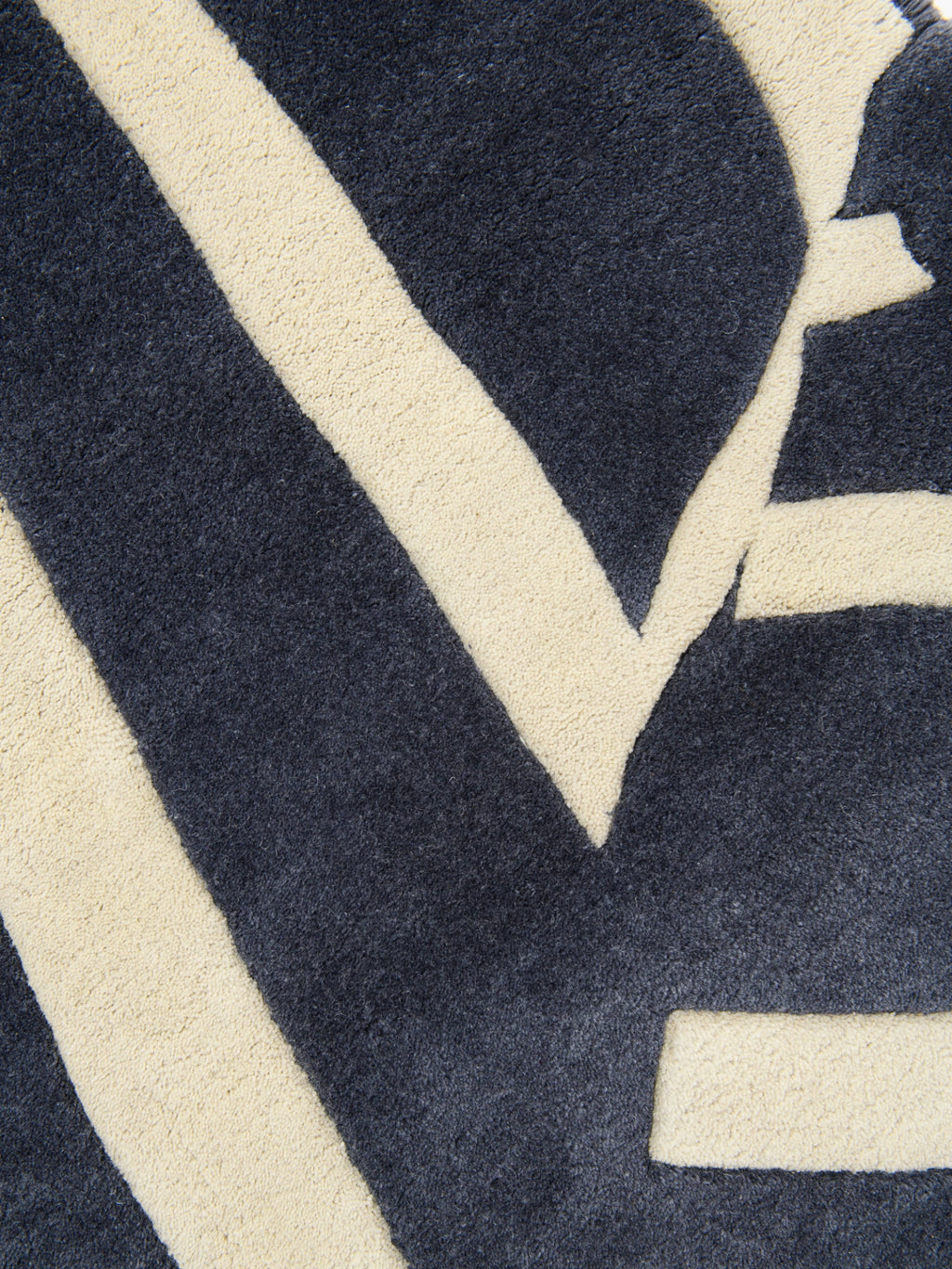 Haus Üger Into the Fold Rug, a modern geometric area rug featuring a striking abstract pattern of thick cream-colored lines against a deep charcoal grey textured wool pile. The plush cream elements contrast with the slightly shorter dark grey pile, creating a dynamic graphic design. Ideal for adding a bold contemporary statement to minimalist living rooms, modern bedrooms, or stylish home office spaces.