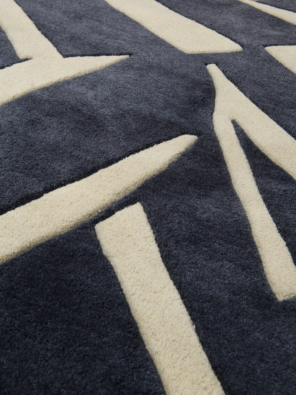 Haus Üger Into the Fold Rug, a modern abstract area rug featuring a bold geometric pattern in deep charcoal grey and soft cream tones.