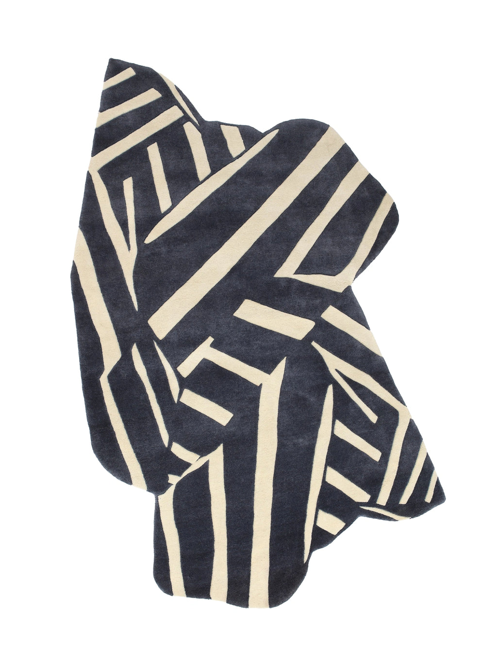 Haus Üger Into the Fold Rug, an abstract area rug with a unique irregular free-form shape, featuring a bold geometric pattern of thick cream-colored stripes against a deep navy blue background. This plush, hand-tufted wool rug provides a soft texture and striking visual interest. Ideal for contemporary living rooms, modern bedrooms, or design-forward spaces looking for a statement floor covering.