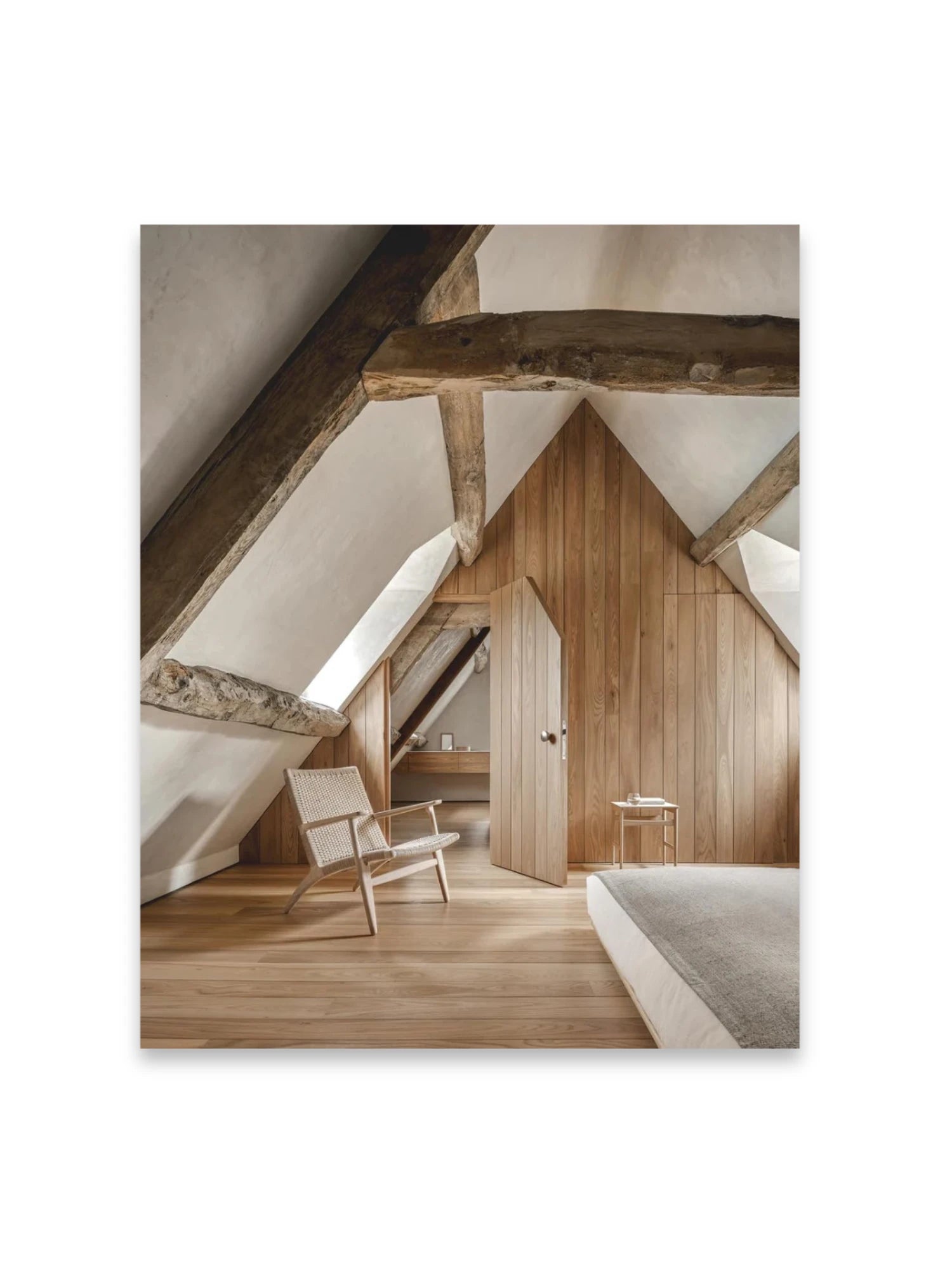 Book In Focus, a beautifully composed image of a rustic modern attic bedroom featuring exposed dark wooden beams, light wood paneling, and a woven armchair. This inspiring book is ideal for interior design enthusiasts and homeowners seeking elegant, natural decor ideas.