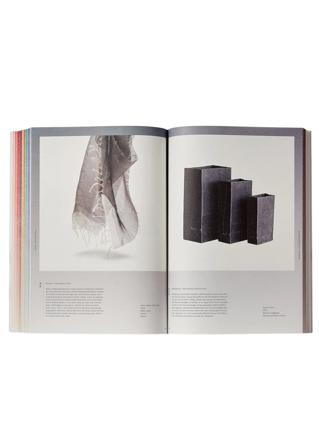 Book Iro - The Essence of Color in Japanese Design, an open, premium hardcover book showcasing vibrant Japanese color swatches along the spine and detailed pages with images of a sheer grey textile and three dark grey paper bags. This visually rich art and design book is perfect for artists, designers, and cultural enthusiasts exploring traditional Japanese aesthetics.