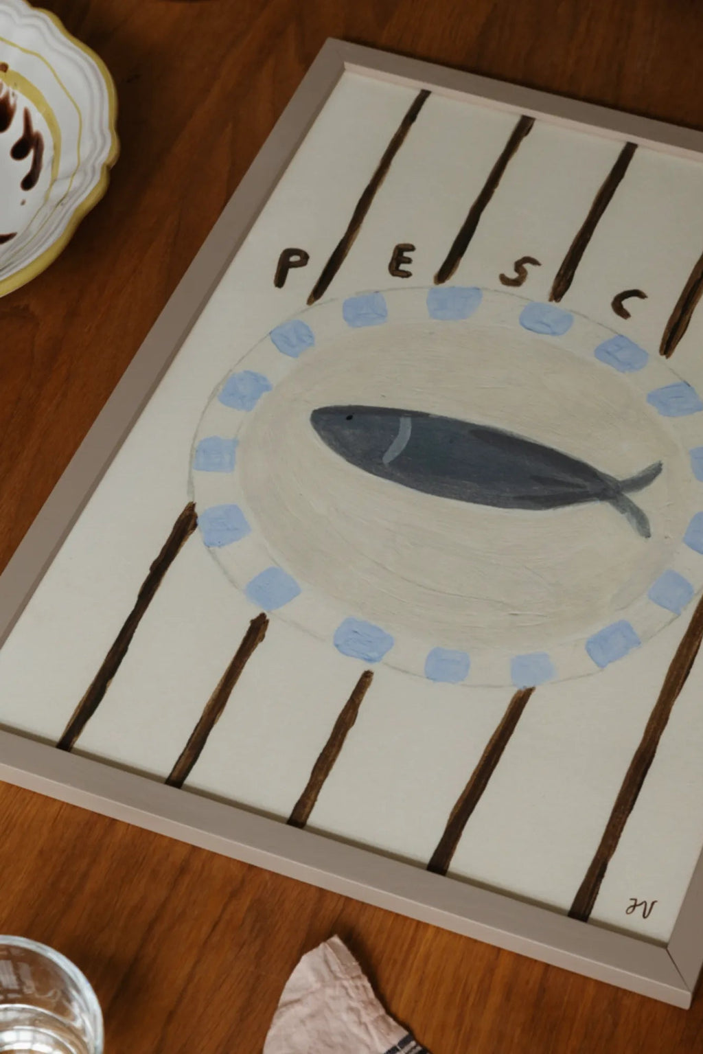 The Poster Club Pesce, a charming folk art print featuring a hand-painted grey-blue fish on a cream-colored oval plate with light blue accents, set against a background of dark brown vertical stripes and "PESC" text.
