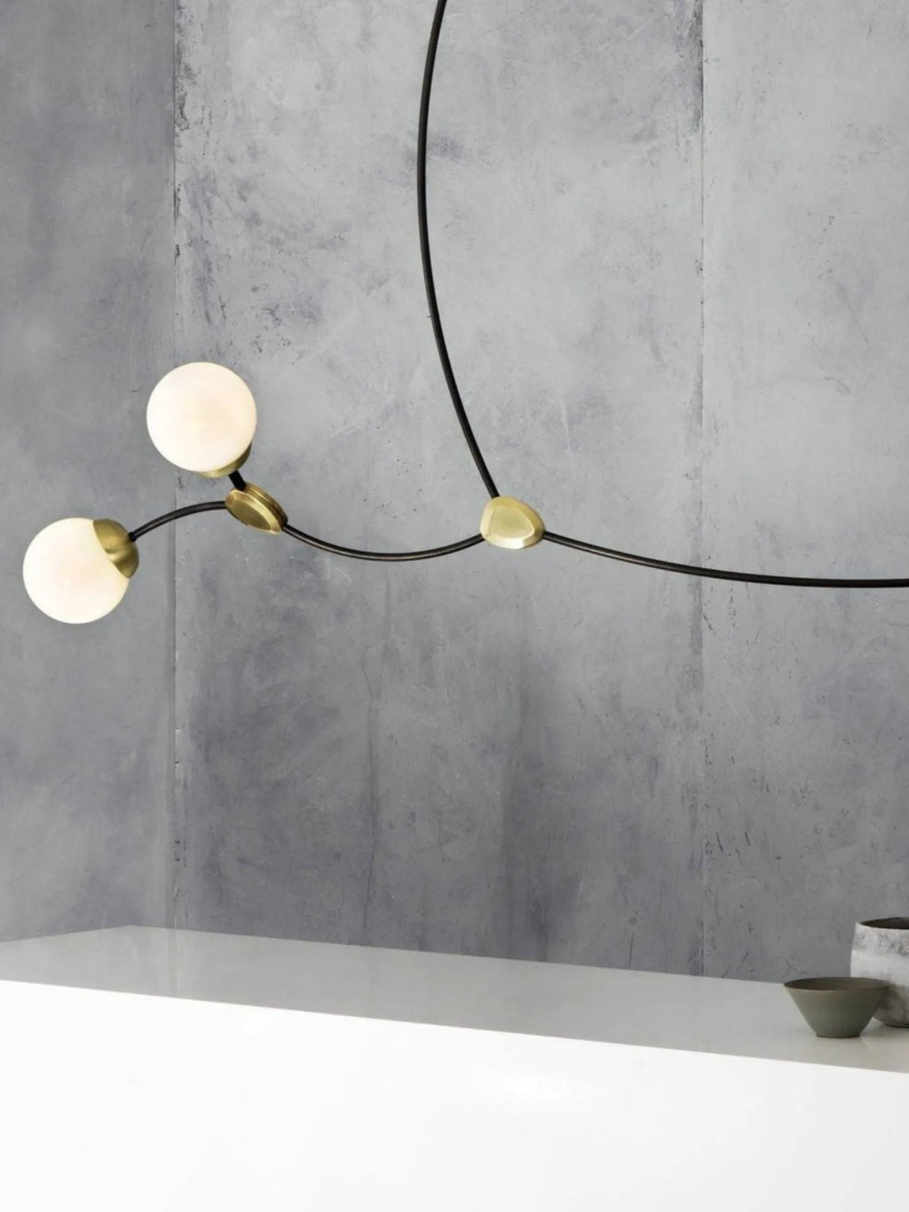 CTO Lighting Ivy 3 Pendant Lamp, featuring three glowing spherical opaline glass shades mounted on elegant dark bronze arms with luxurious polished brass accents, against a textured gray wall. This stylish modern ceiling light offers sophisticated illumination for contemporary living spaces and discerning homeowners.