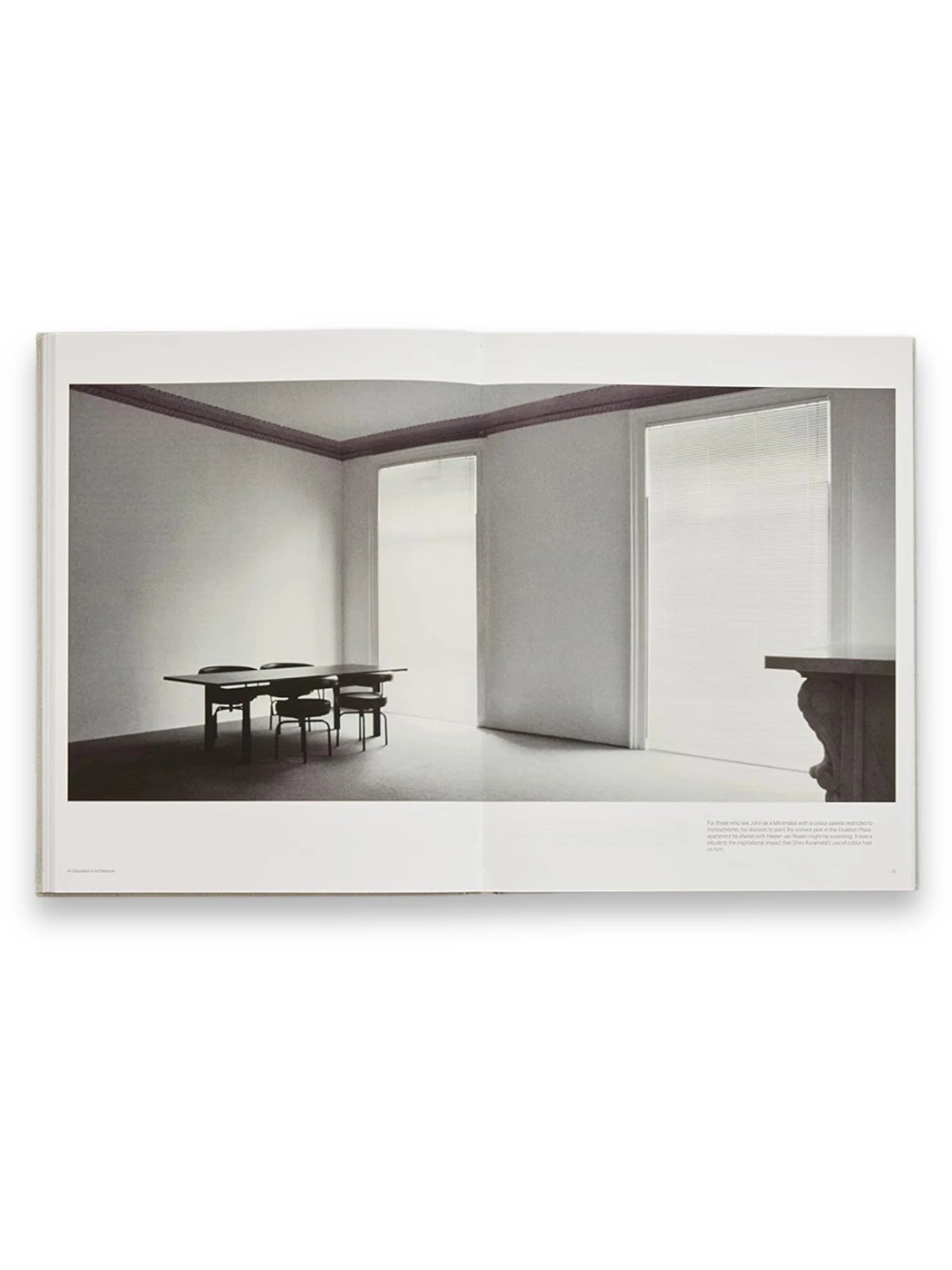 Book John Pawson - Making Life Simpler, an open book displaying a minimalist interior photograph in black and white. The image shows a spacious room with a dark dining table and chairs, contrasting light walls, and large windows with blinds, embodying modern architectural design. This inspiring architecture book is perfect for design enthusiasts, students, and professionals seeking minimalist aesthetic ideas and creative inspiration.