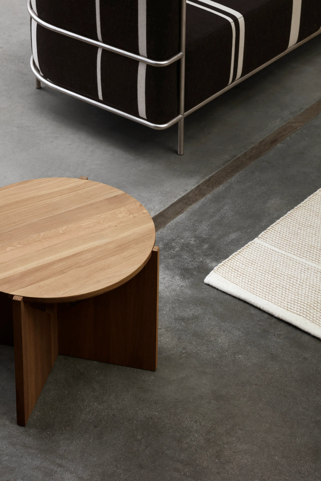 Kristina Dam Simple Coffee Table, a modern minimalist round coffee table crafted from light natural solid oak, featuring a smooth wood grain tabletop and a striking geometric base with intersecting dark oak panels. Perfect for adding Scandinavian design and organic modern elegance to a contemporary living room or lounge area.