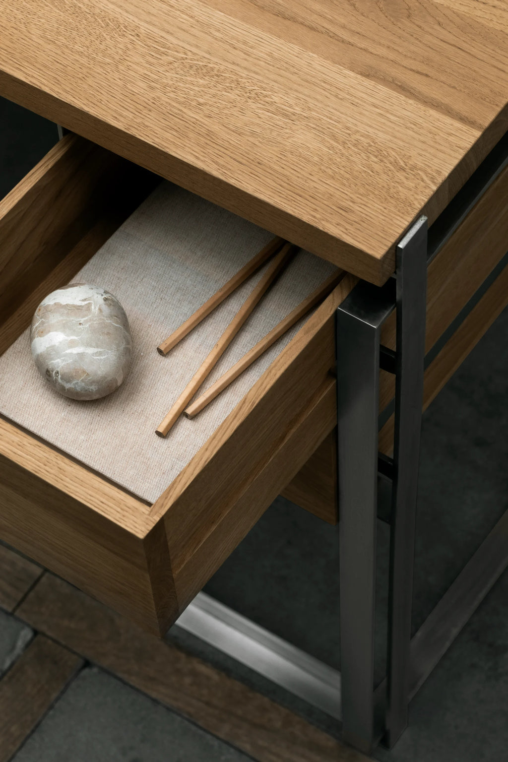 Kristina Dam Outline Desk, a modern minimalist desk featuring a natural solid oak top and an integrated drawer with a light beige fabric liner, all supported by a sturdy matte black metal frame. This Scandinavian design piece offers clean lines and functional storage, perfect as a stylish home office desk or a contemporary console table for living rooms and entryways.