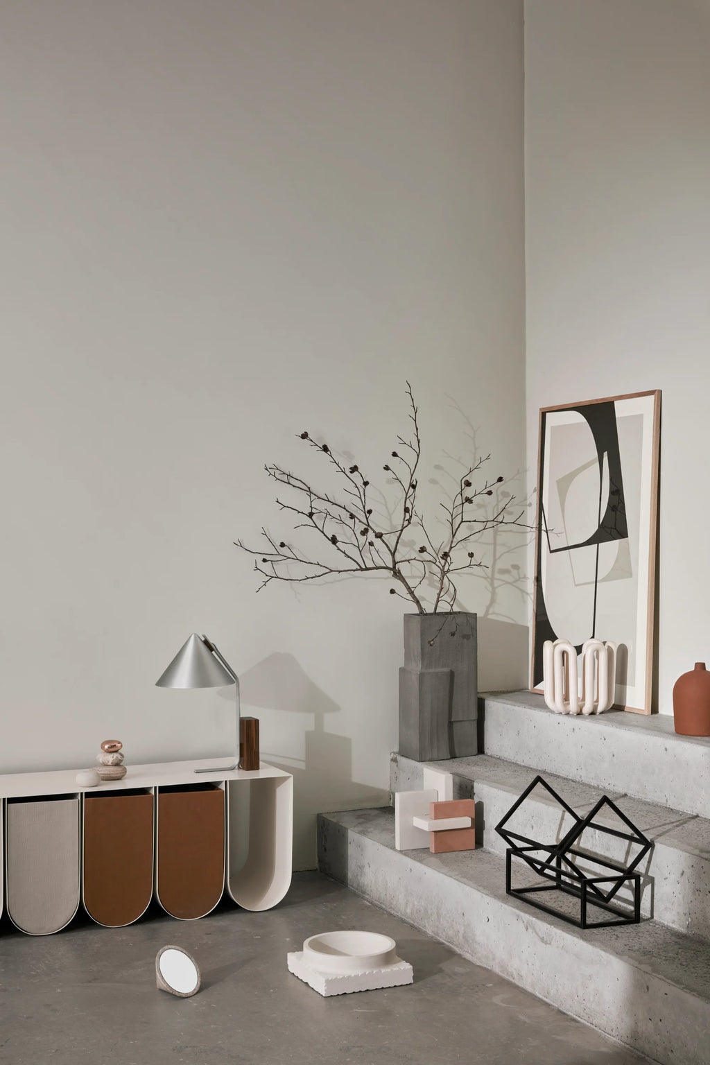 Kristina Dam Monolith Vase, a grey brutalist concrete vase with a raw, textured finish and a striking geometric, sculptural form resembling stacked blocks. This industrial-chic decorative object is perfect for modern minimalist shelf styling or as a contemporary entryway statement piece.