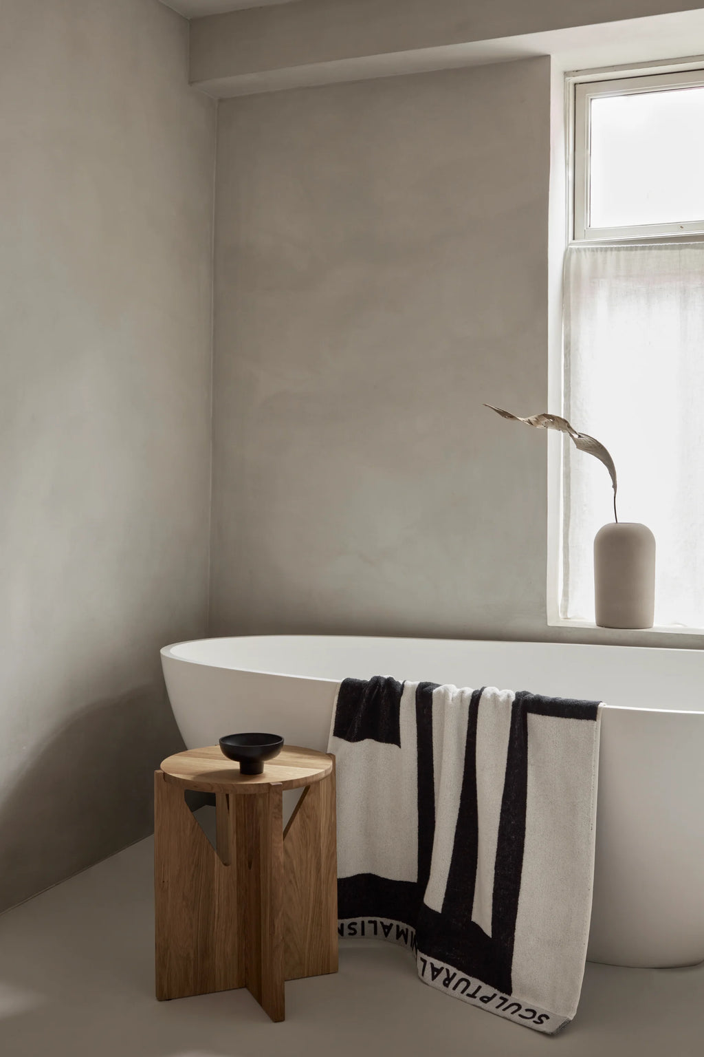 Kristina Dam Simple Stool, a minimalist solid oak stool crafted from natural wood with a smooth cylindrical top and a unique geometric base featuring triangular cut-outs, showcasing a clean Scandinavian design. This versatile wooden accent stool functions beautifully as a modern side table for organic modern bathrooms or contemporary living rooms.