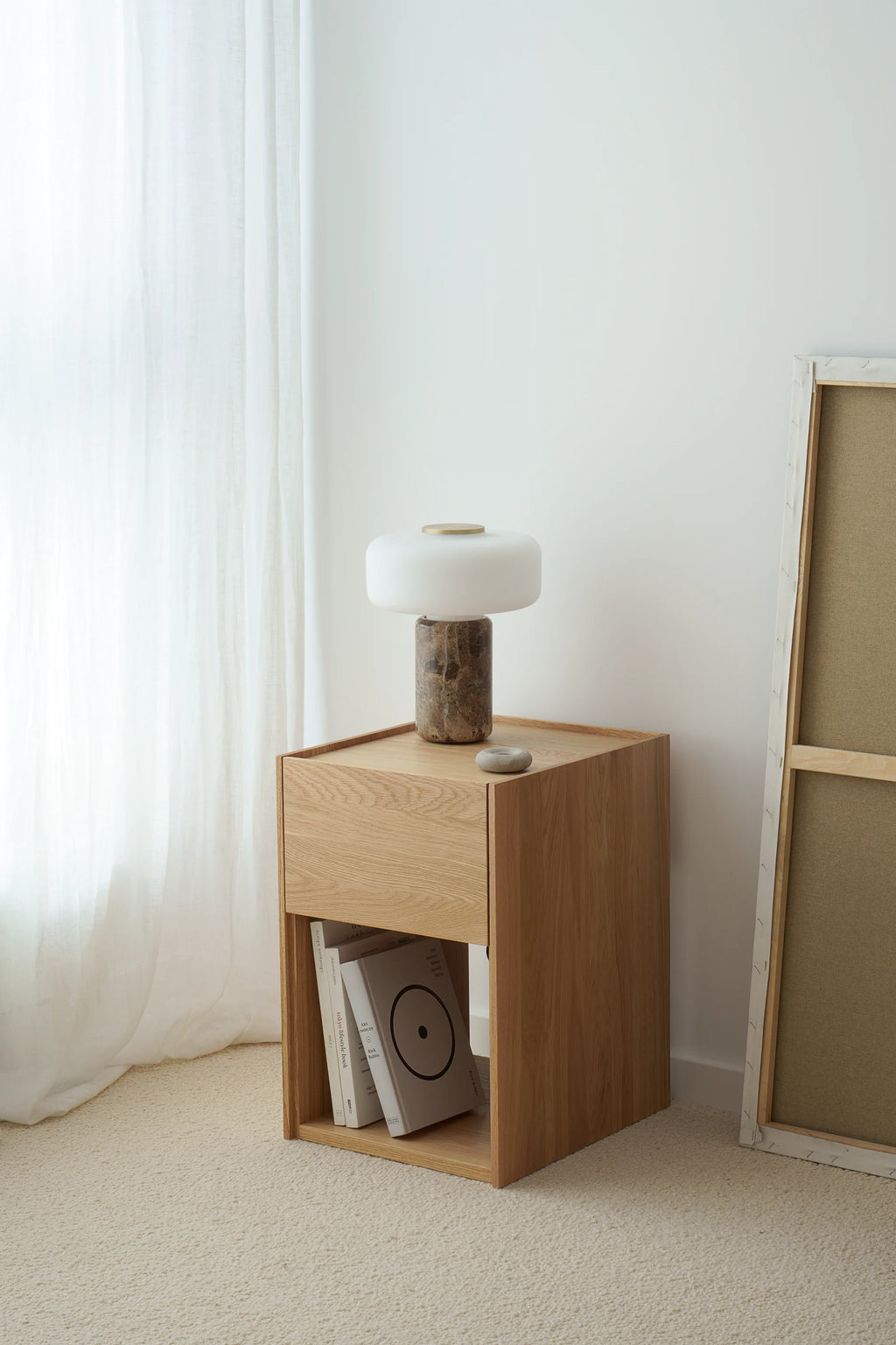 TAMO Kari Nightstand, a premium light oak wood nightstand with a floating drawer and an open lower shelf for books, styled with a modern lamp. Ideal for contemporary bedroom storage.