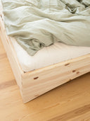 close up photo of the orbit bed by karup design, the photo features a wooden bed frame, a white mattress with a blanket on it