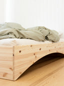close up photo of the orbit bed by karup design, the photo features a wooden bed frame, a white mattress with a blanket on it. showcases the arch that gives the bed a floating feel