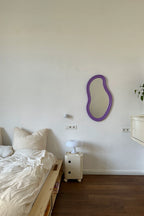 Bedroom with a purple mirror on the wall, a nightstand with a lamp, and a bed.