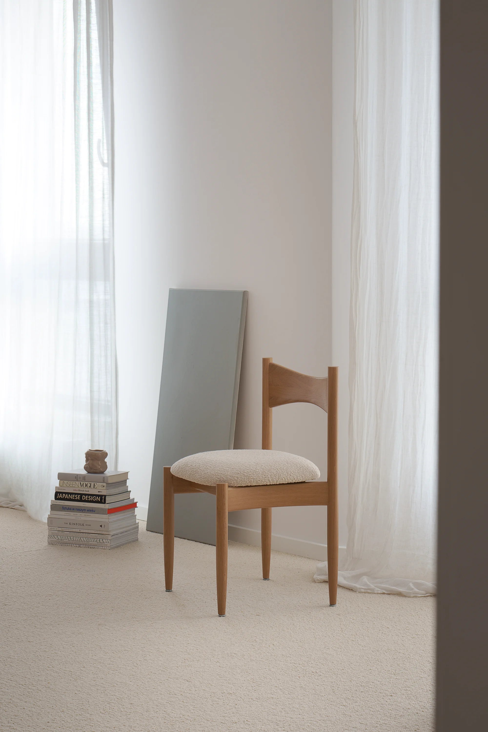 Wooden chair with a white cushion in a minimalistic room with light curtains.