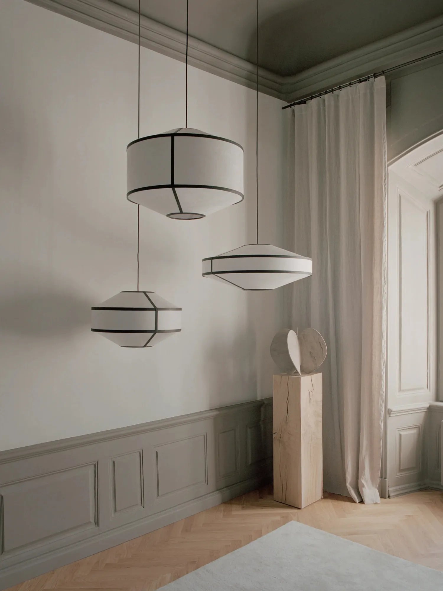 New Works Kite Pendant Lamp; three unique white fabric drum and faceted lamps with black frames, displayed in a modern, neutral room. A premium statement lighting piece.