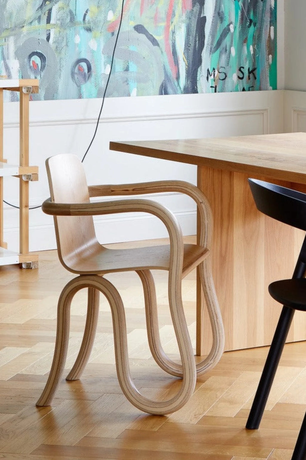 Made by Choice Kolho Dining Chair, a stylish and modern chair crafted from light natural bent plywood, featuring distinctive curved legs and armrests, placed beside a wooden dining table in a contemporary room.