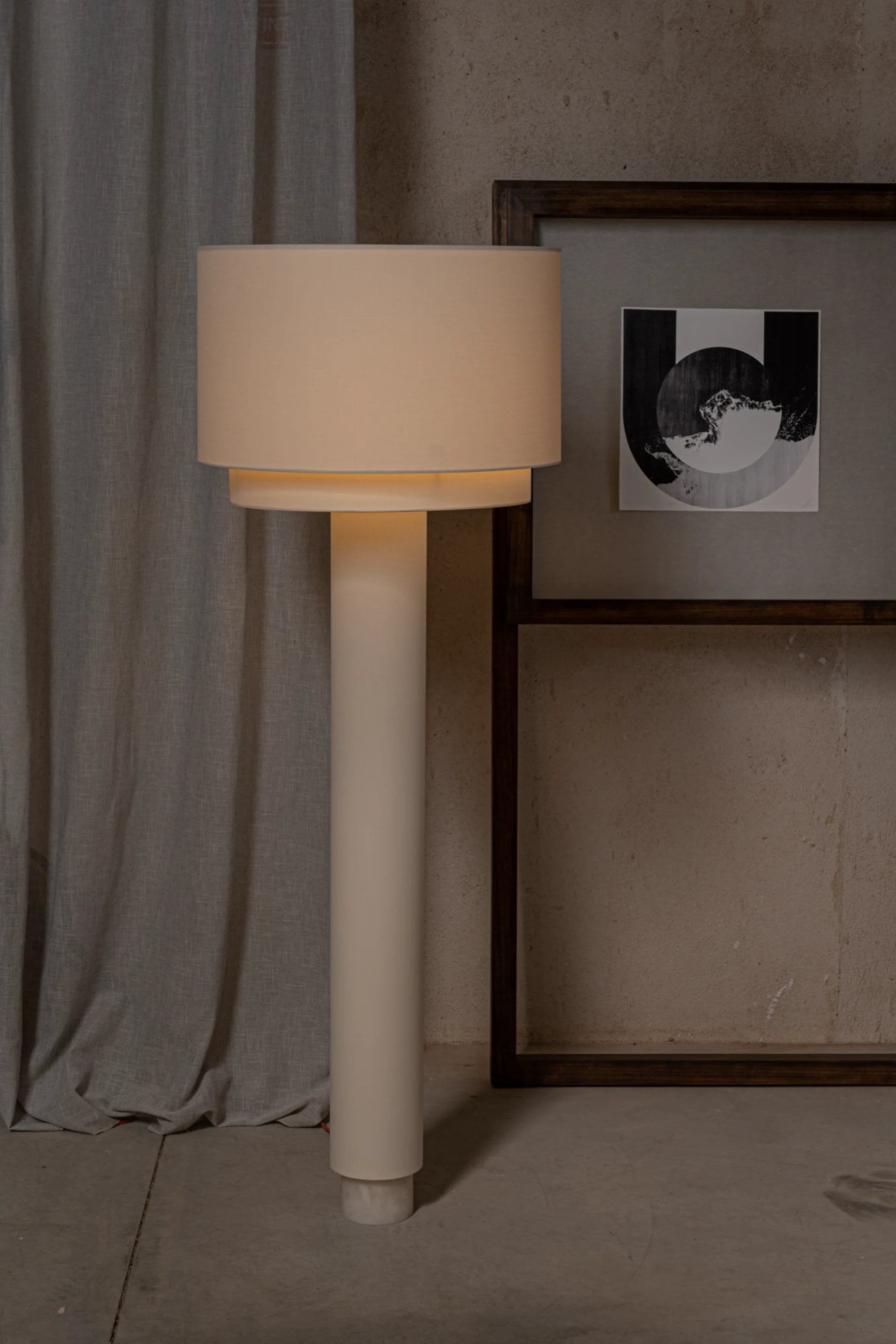 Beige floor lamp against a neutral wall with a framed picture.