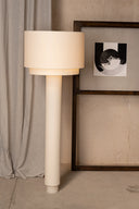 Beige floor lamp against a neutral wall with a framed picture.