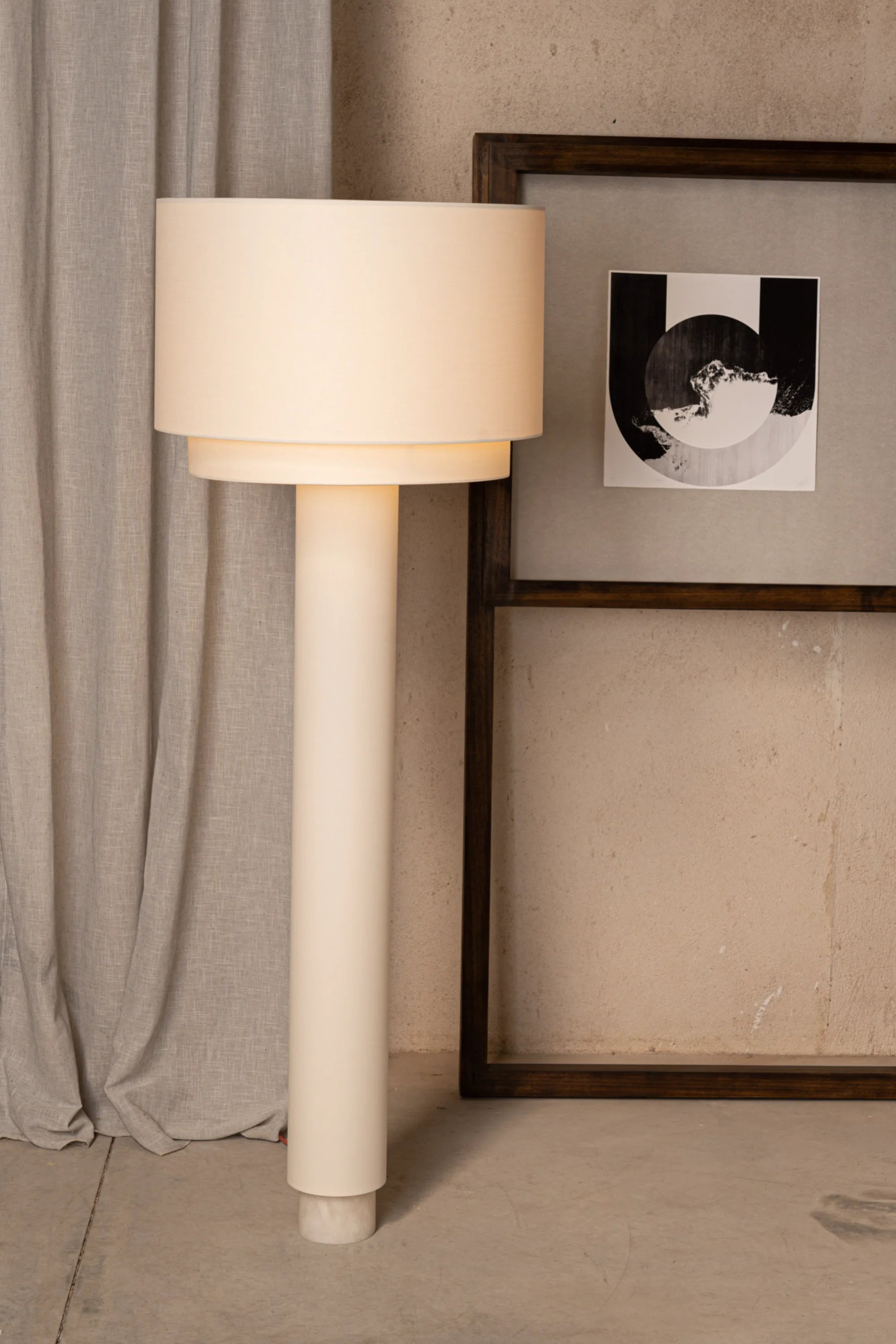 Beige floor lamp against a neutral wall with a framed picture.