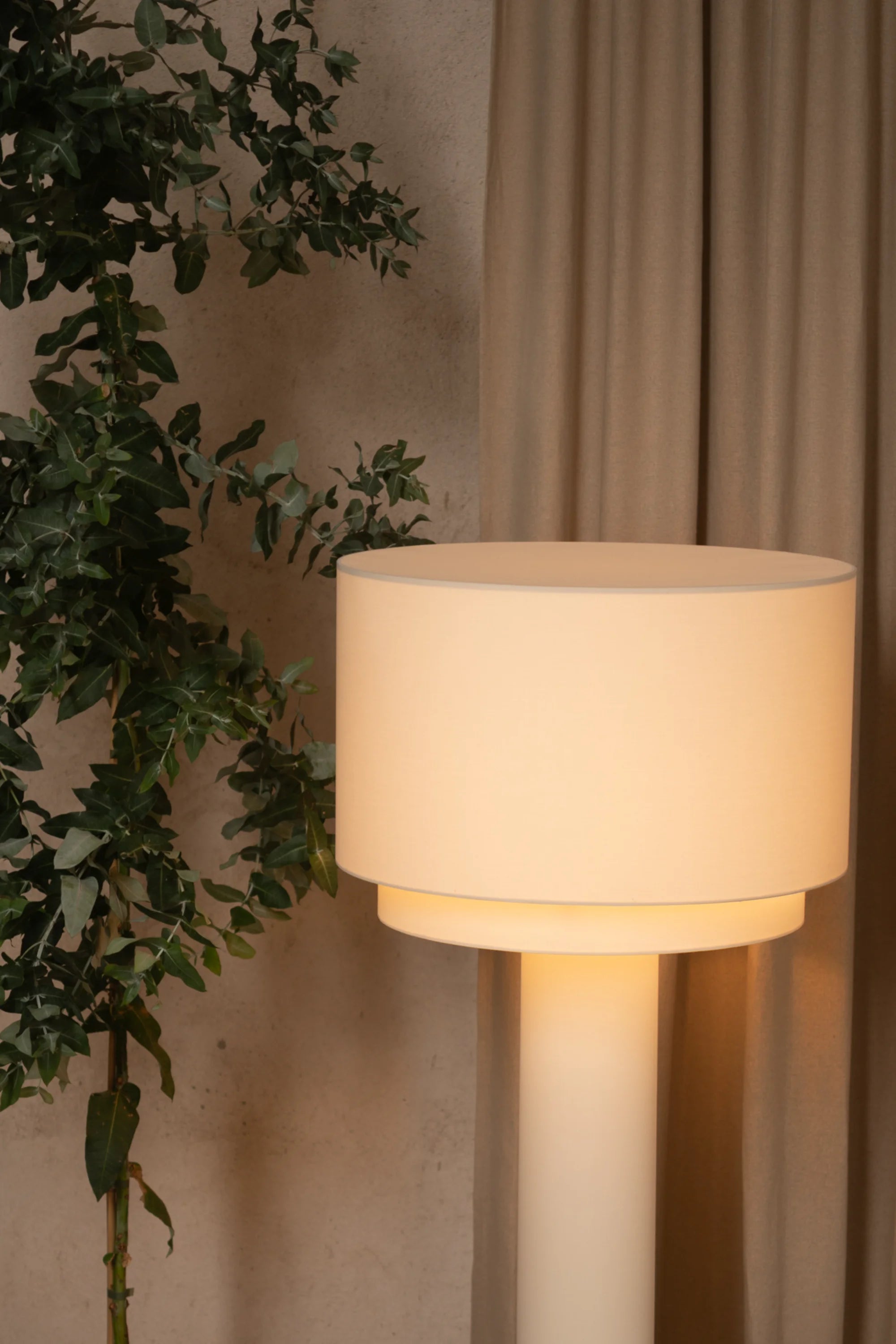 Floor lamp with a beige shade next to a plant against a beige wall