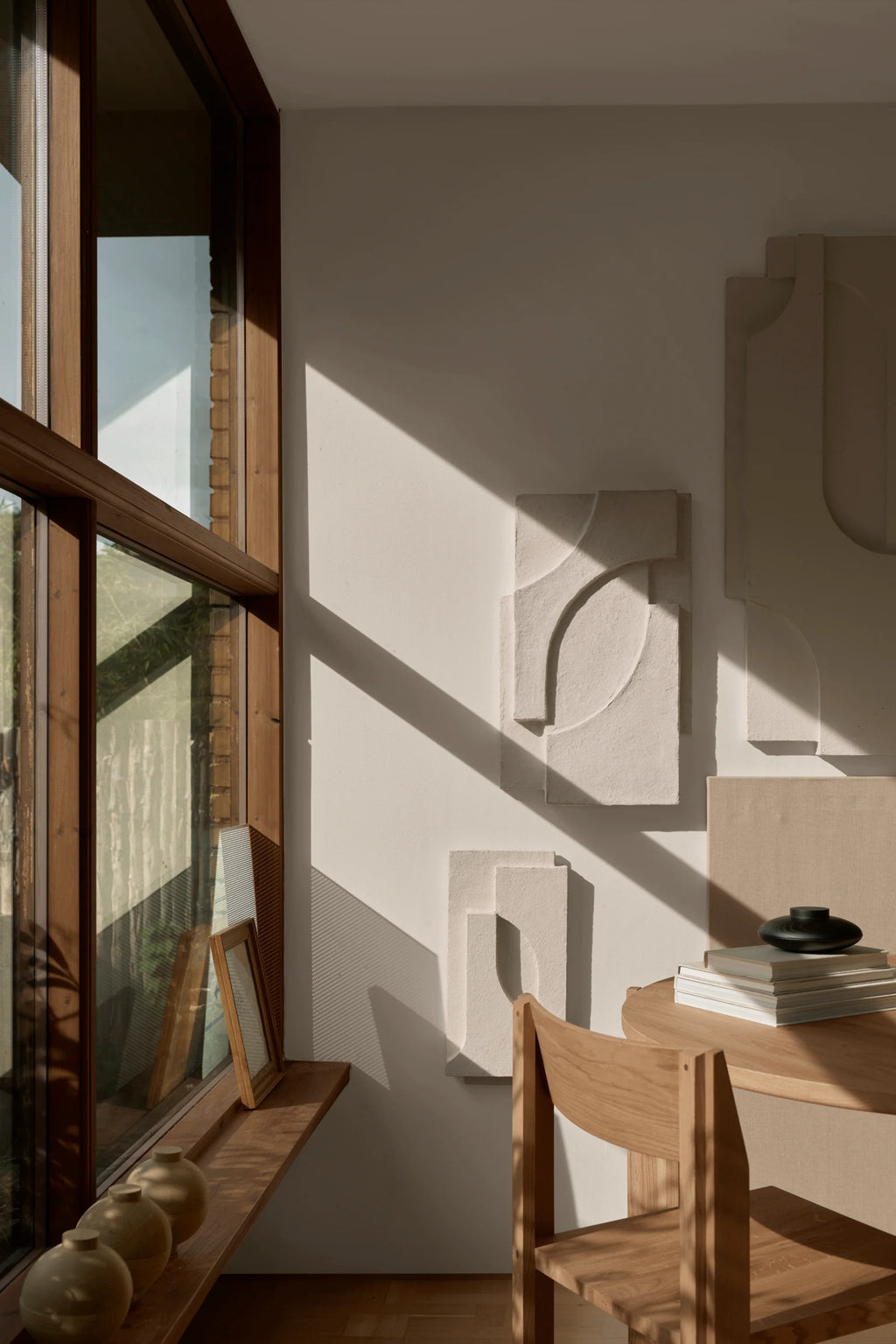 Kristina Dam Serif Relief M, a modern minimalist sculptural wall art piece featuring a rectangular panel with a raised, textured relief of geometric and organic curved shapes in a creamy off-white. Crafted from a durable mineral composite, its raw, tactile surface creates dynamic shadows and architectural depth.