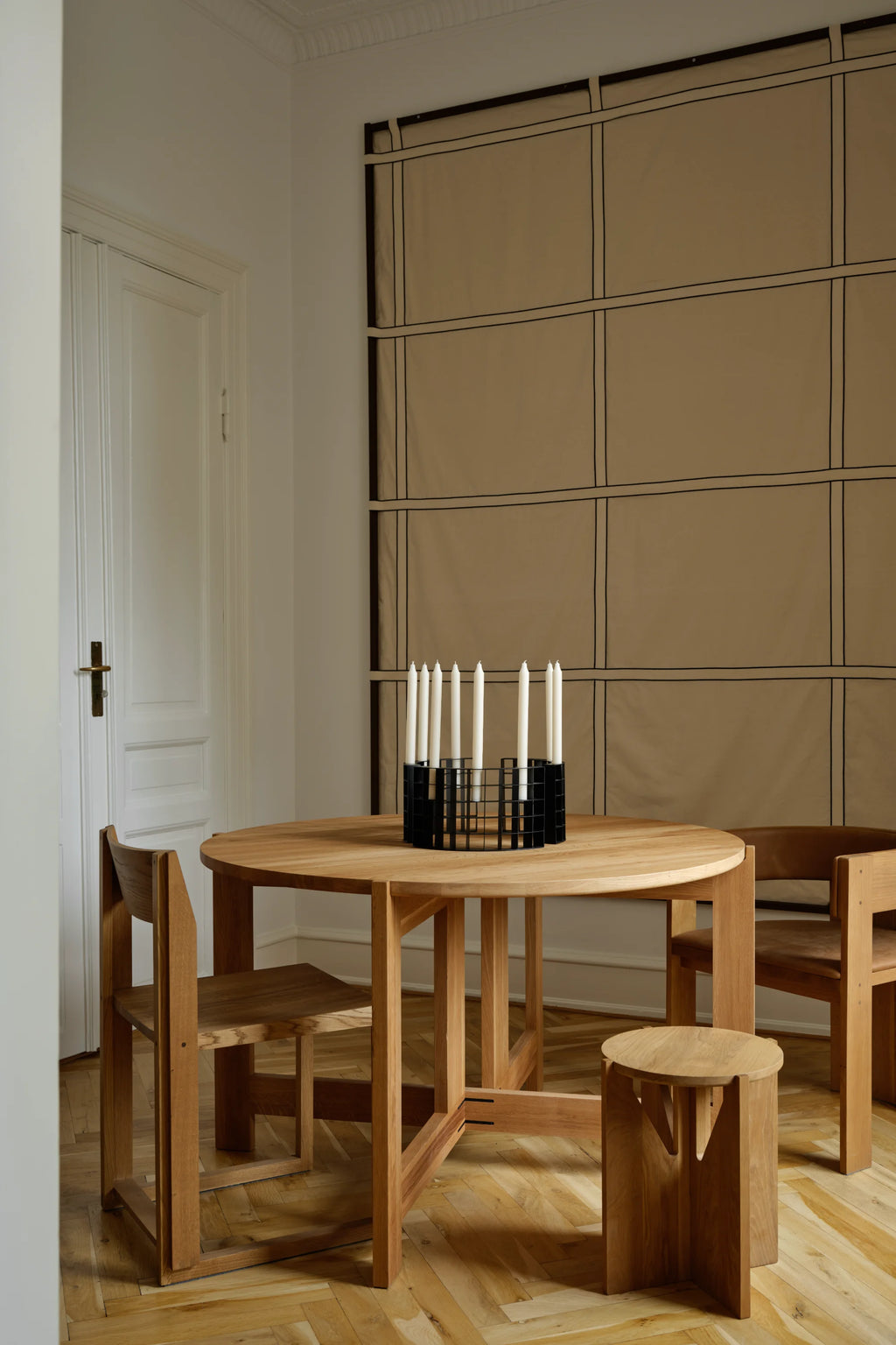 Kristina Dam Simple Stool, a modern minimalist round-seated stool crafted from natural solid oak wood, featuring a light wood finish and a distinctive geometric base with architectural vertical panels. This versatile Scandinavian wood stool is ideal as a stylish side table in contemporary living rooms or a functional accent piece for Japandi-inspired bedrooms.