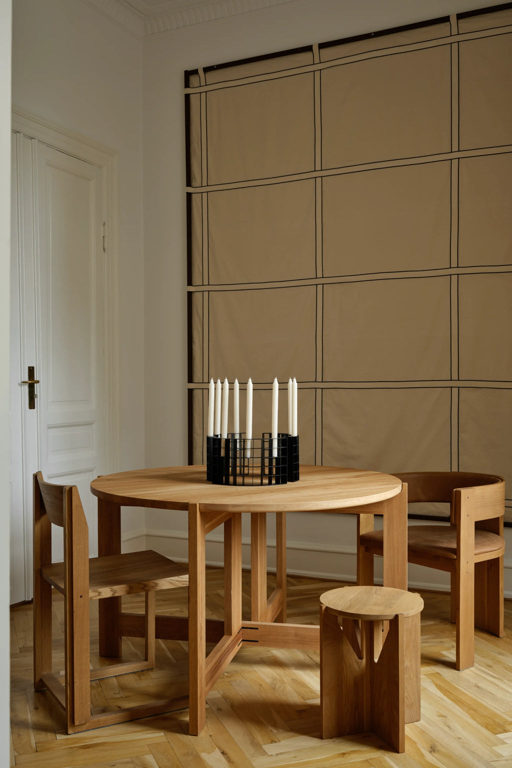 Kristina Dam Mesh Candle Holder, a striking modern minimalist candelabra crafted from matte black powder-coated steel, featuring a unique cylindrical grid design that securely holds multiple tall white candles. This contemporary black metal candle holder makes an ideal Scandinavian dining table centerpiece or a sophisticated accent for modern shelf styling and living room decor.