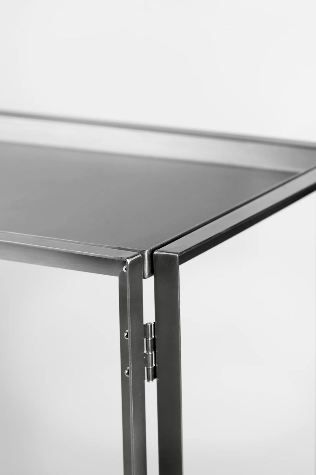 Kristina Dam Foldable Side Table, a sleek modern minimalist side table crafted from brushed stainless steel with a matte silver-grey finish. It features clean rectangular lines, a sturdy frame, and a visible hinge mechanism highlighting its functional, foldable design. This industrial chic metal accent table is perfect for versatile use in contemporary living rooms, minimalist bedrooms, or small apartment spaces.