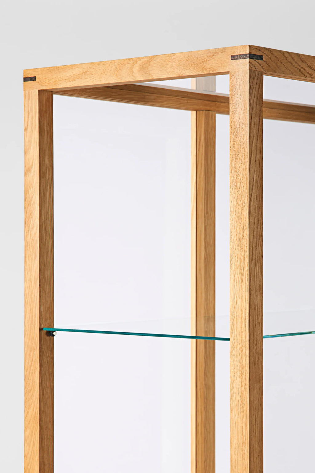Kristina Dam Japanese Cabinet L, a minimalist display cabinet crafted from solid light oak with distinctive dark wood inlay joinery at the corners, featuring sleek clear glass shelves and a clean-lined rectangular frame. This Scandinavian-inspired storage unit offers elegant open shelving for modern living rooms, dining spaces, or sophisticated home offices.