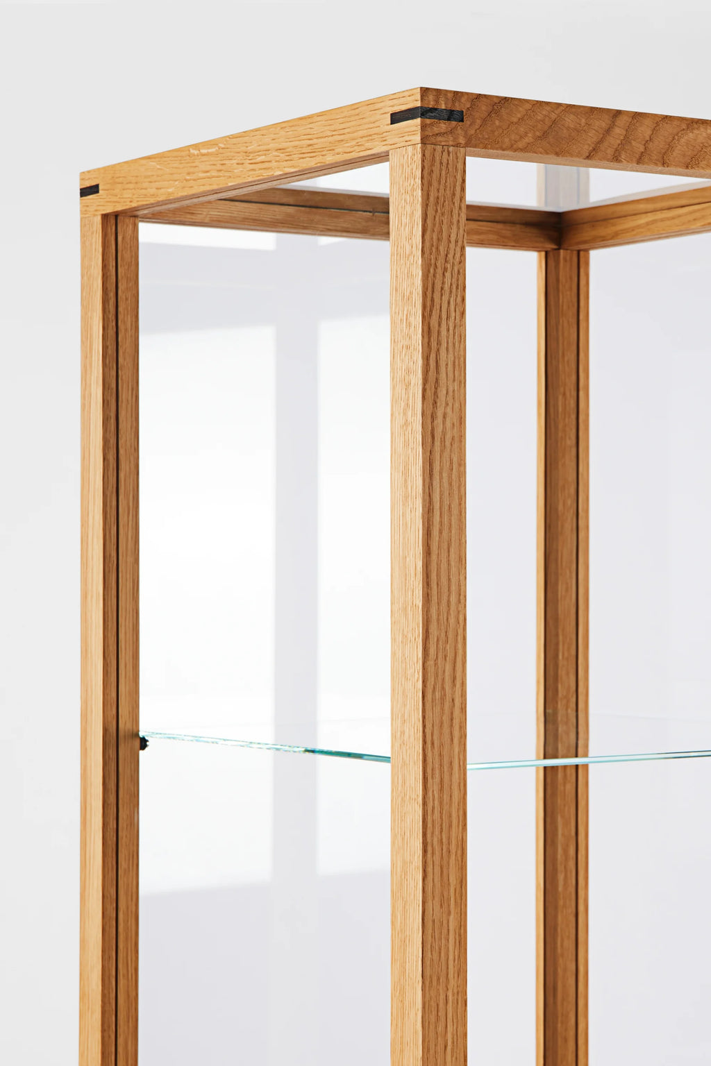 Kristina Dam Japanese Cabinet M, a modern minimalist display cabinet crafted from light natural solid oak with distinctive black Japanese joinery details and clear glass shelves. This tall, rectangular oak shelving unit offers elegant storage for Scandinavian living rooms, Japandi dining areas, or contemporary home offices.